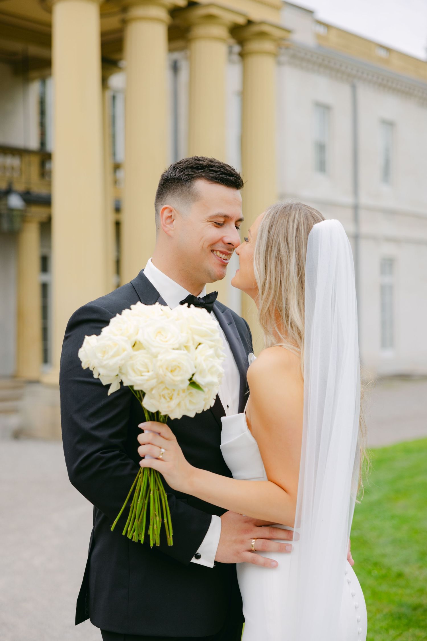 Joyful wedding moment with couple and white bouquet against classical architecture.