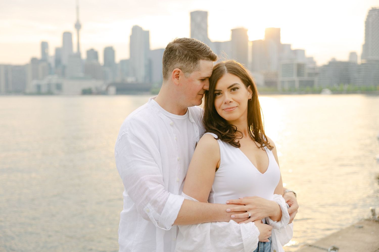 Couple shares intimate embrace with Toronto's majestic skyline glowing in sunset light.