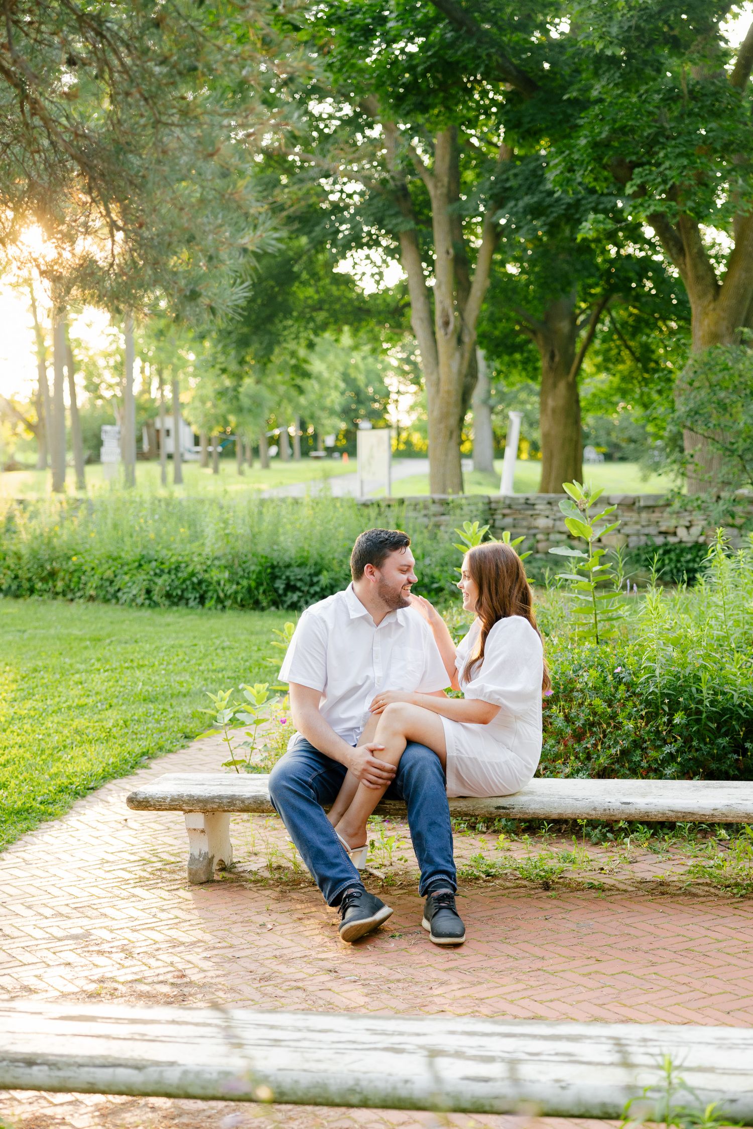 A couple sharing a romantic moment on a stone bench along a brick pathway in a park.
