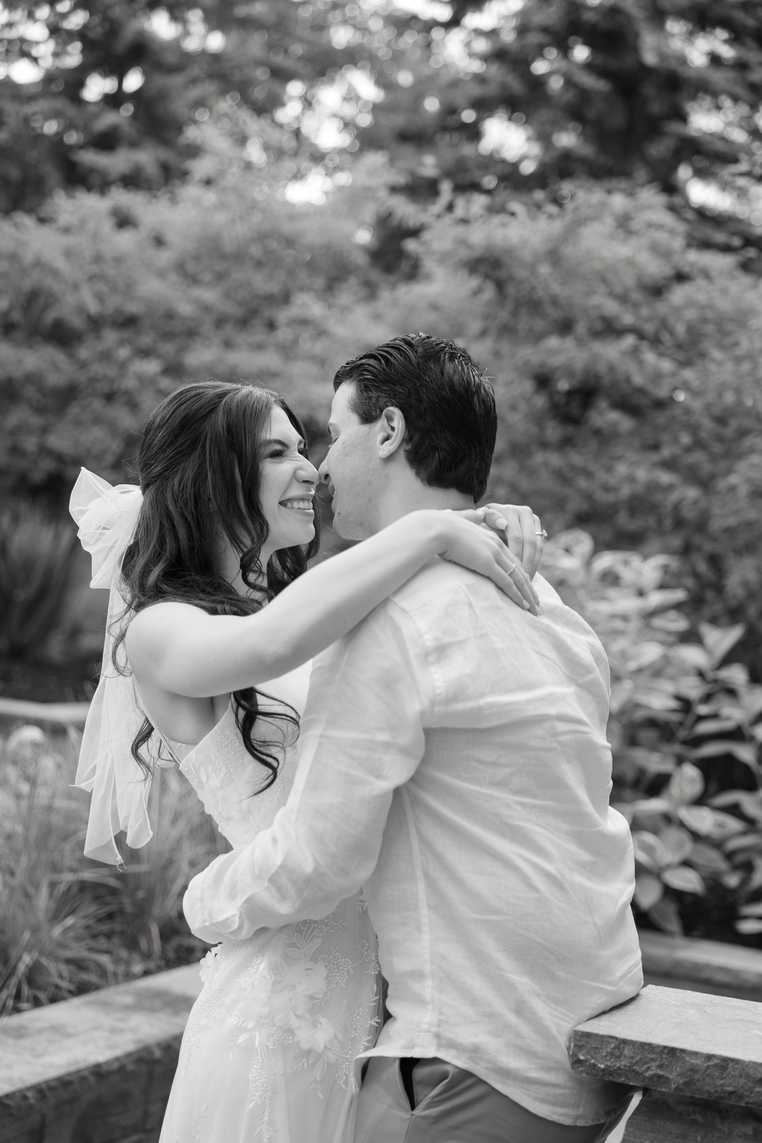 A black and white wedding photo capturing a joyful embrace in a garden setting.