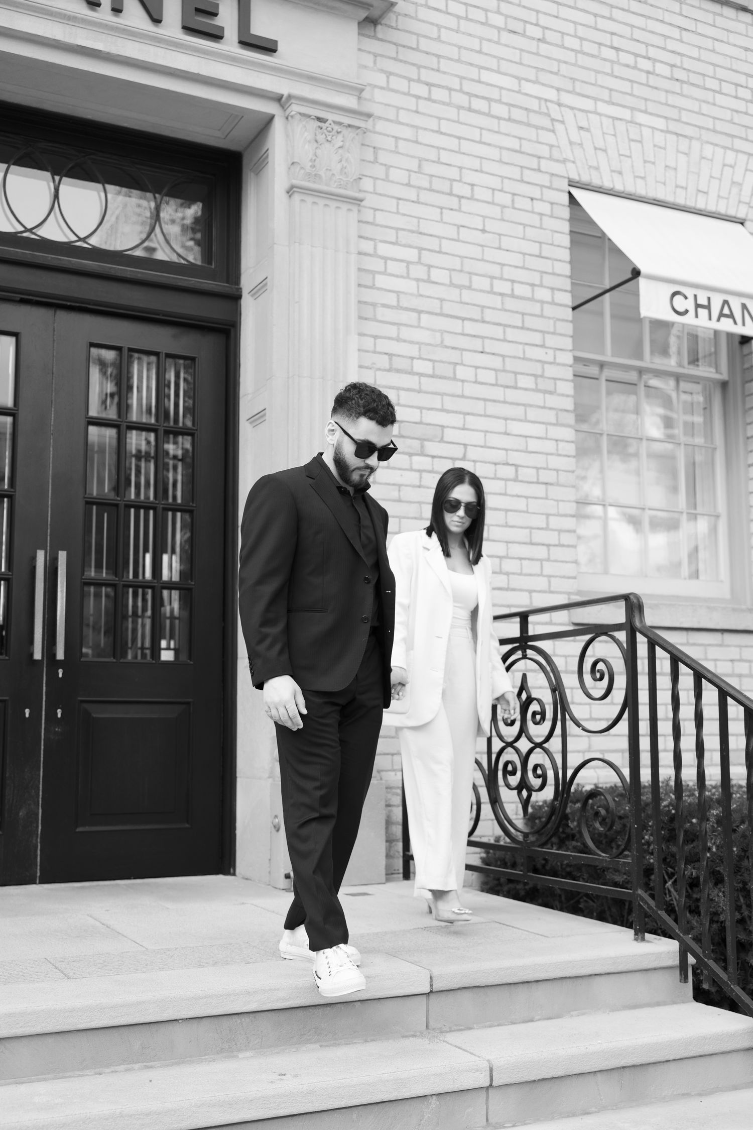 Black and white photo of a couple in formal attire standing on stone steps near a Chanel store.