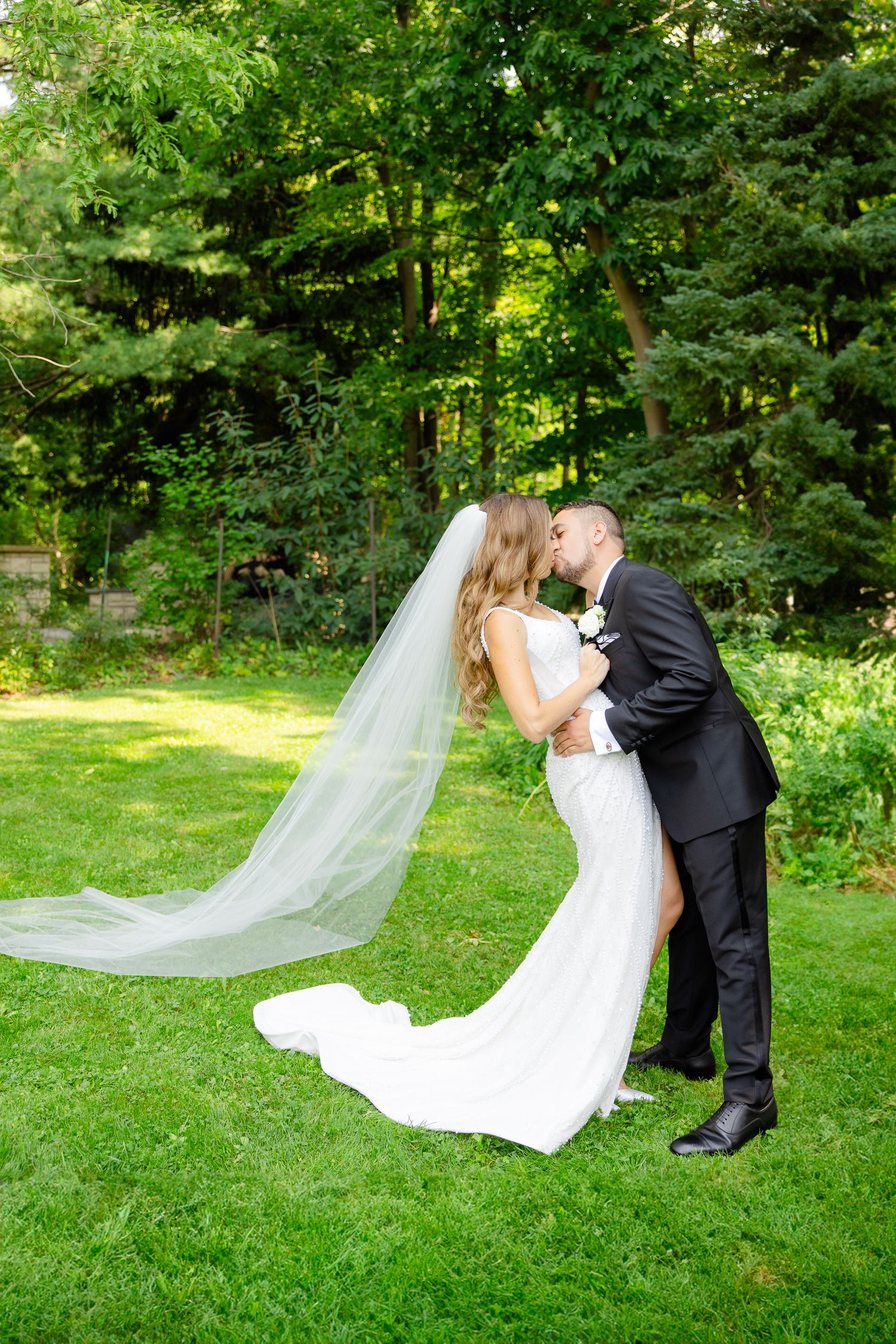 An elegant wedding photo capturing a romantic kiss with a flowing veil in a garden setting.