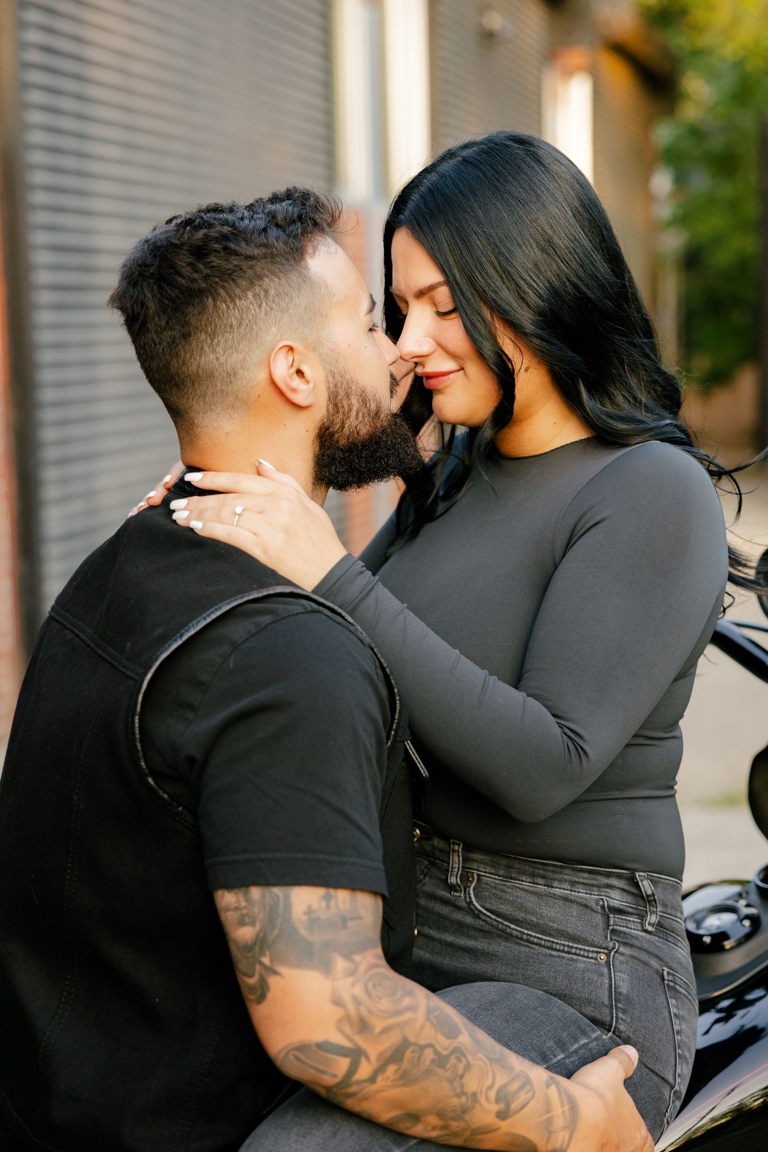 A couple shares a romantic moment on a motorcycle during an outdoor photoshoot.