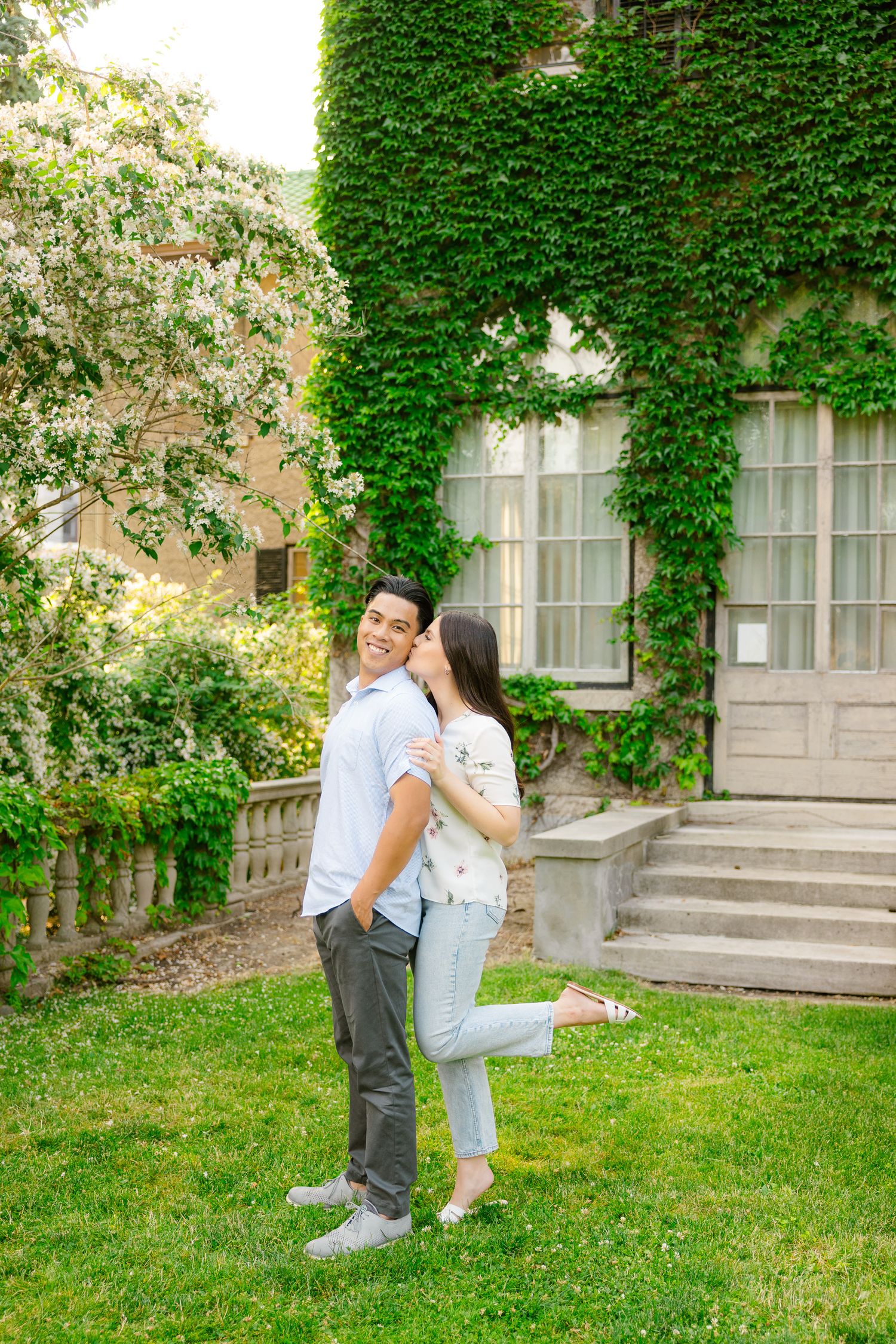 A romantic couple embraces in front of an ivy-covered building during a spring photoshoot.