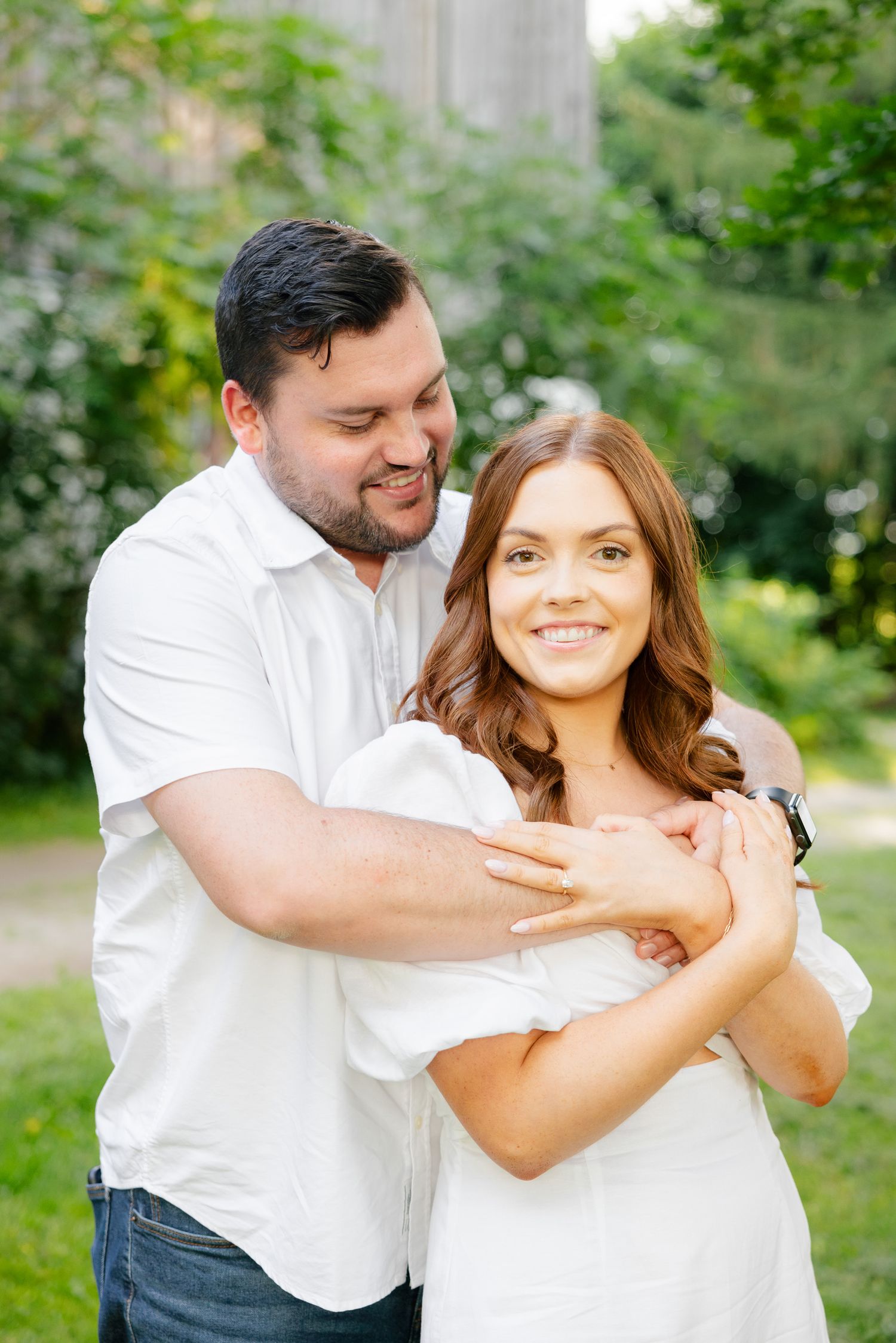 A romantic couple in white outfits embracing outdoors in a garden setting with green foliage in the background.