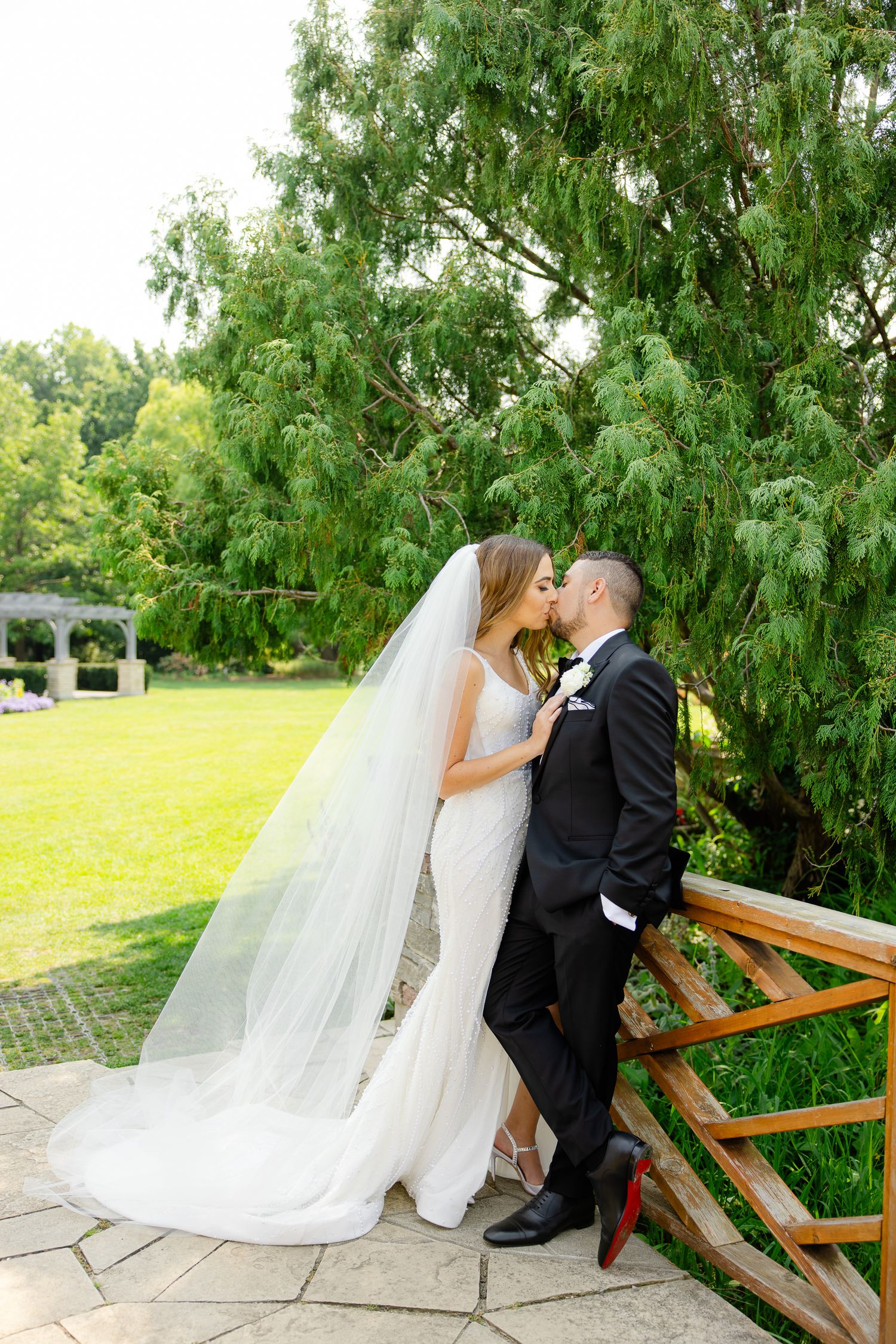 Romantic moment captured between newlyweds by wooden railing in garden setting.