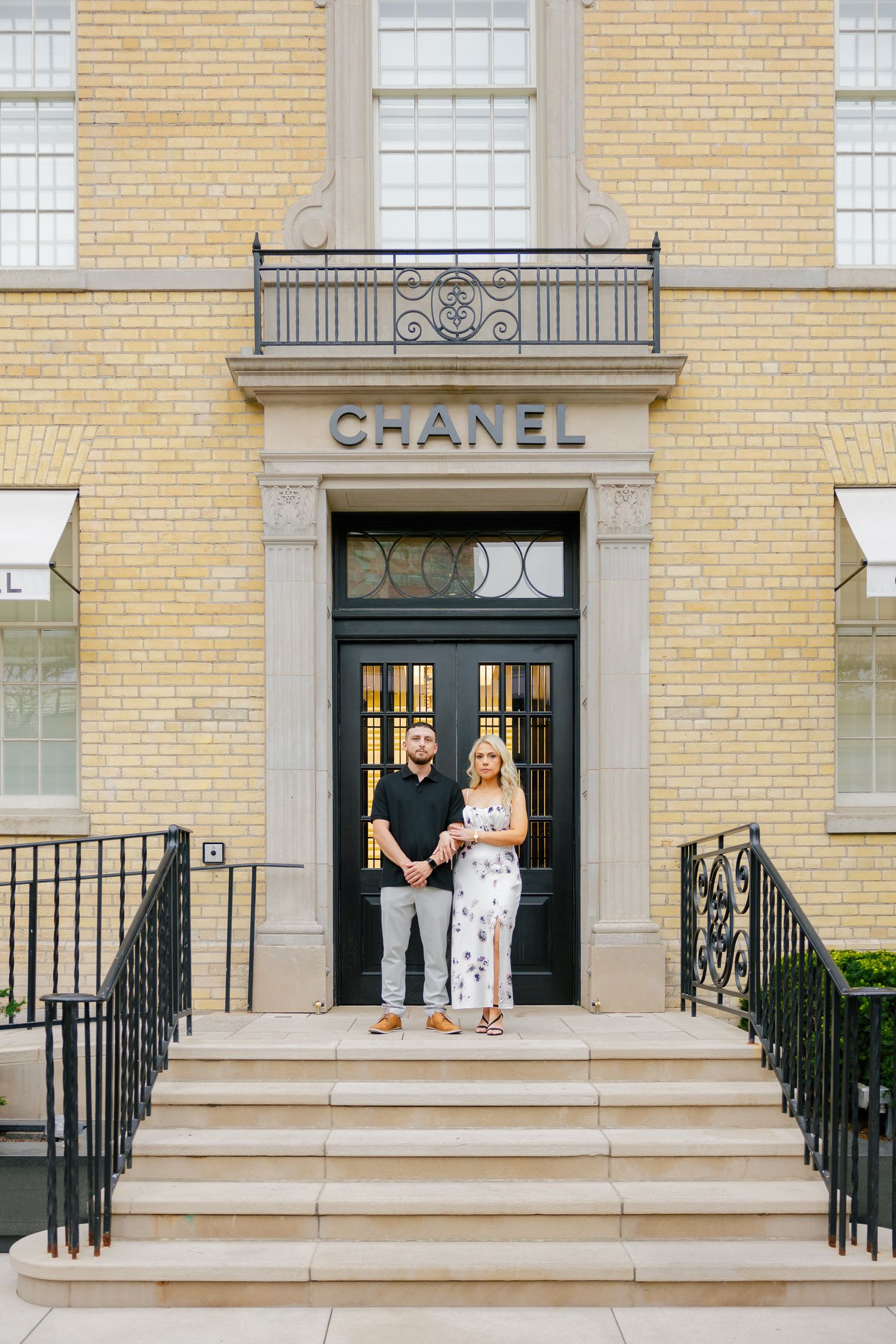 A couple poses in front of a Chanel store entrance with classic yellow brick architecture.