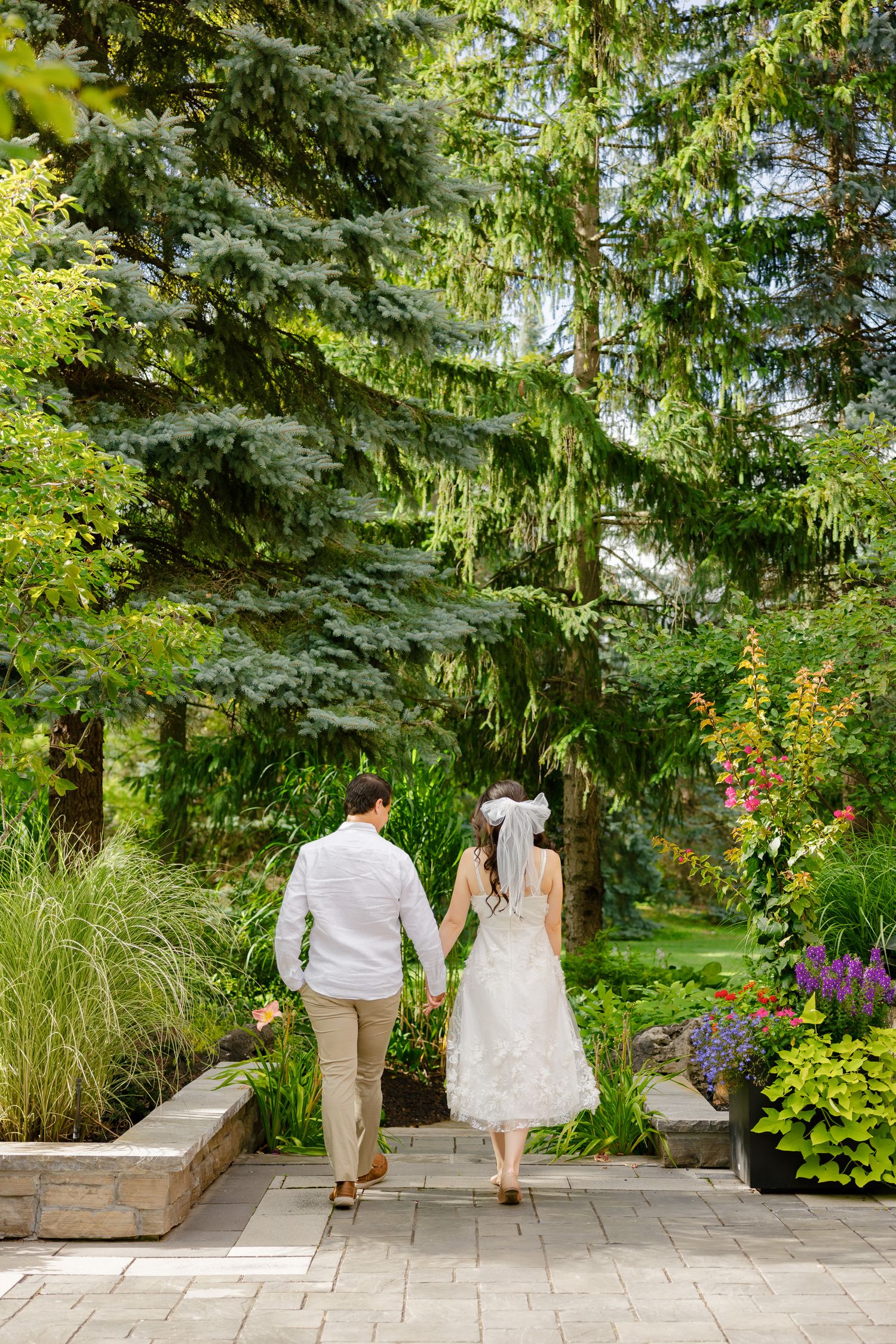 Wide shot of newlyweds walking away on a stone path surrounded by lush garden landscaping.