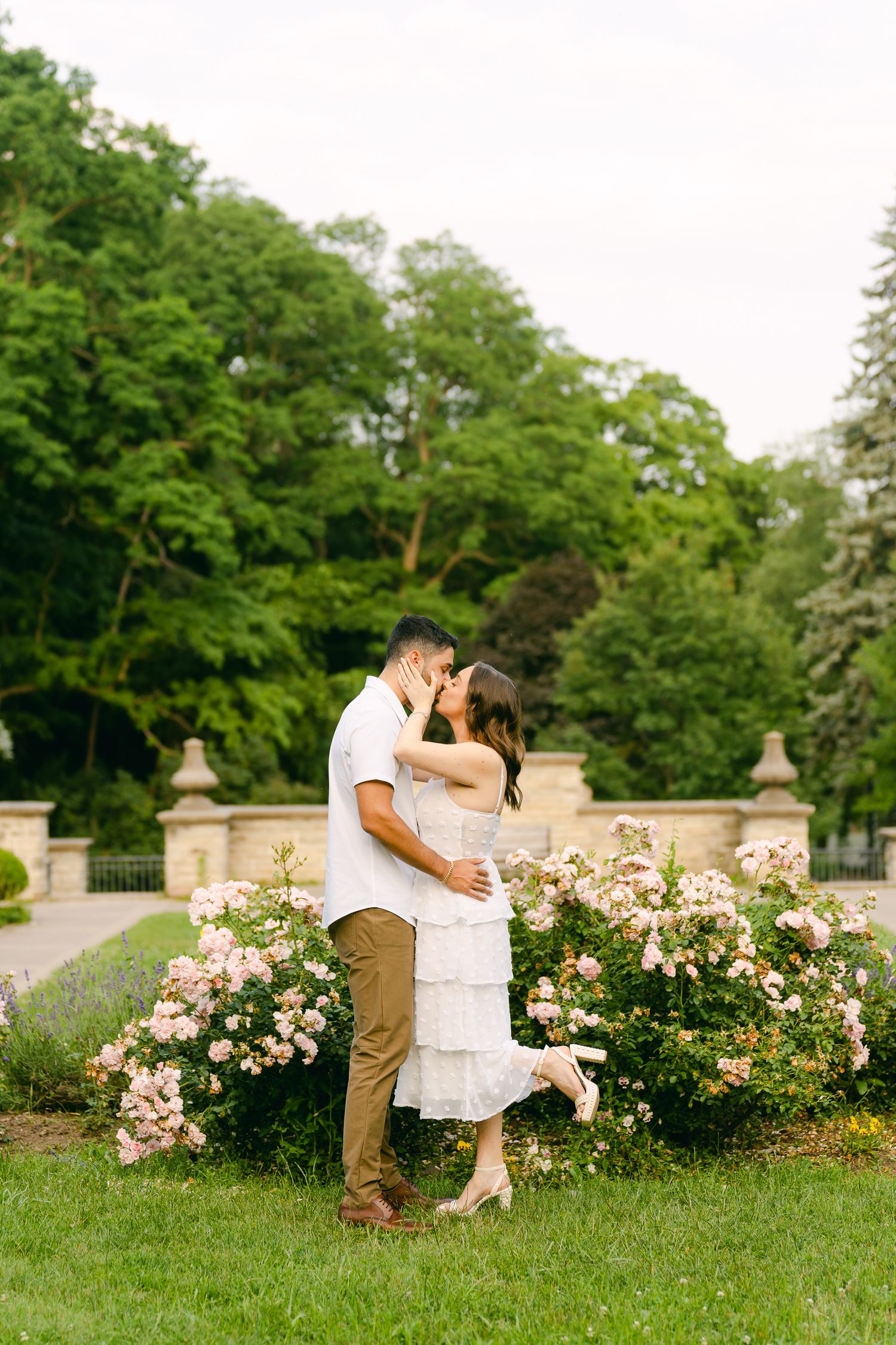 A romantic embrace among blooming rose bushes in a formal garden setting.