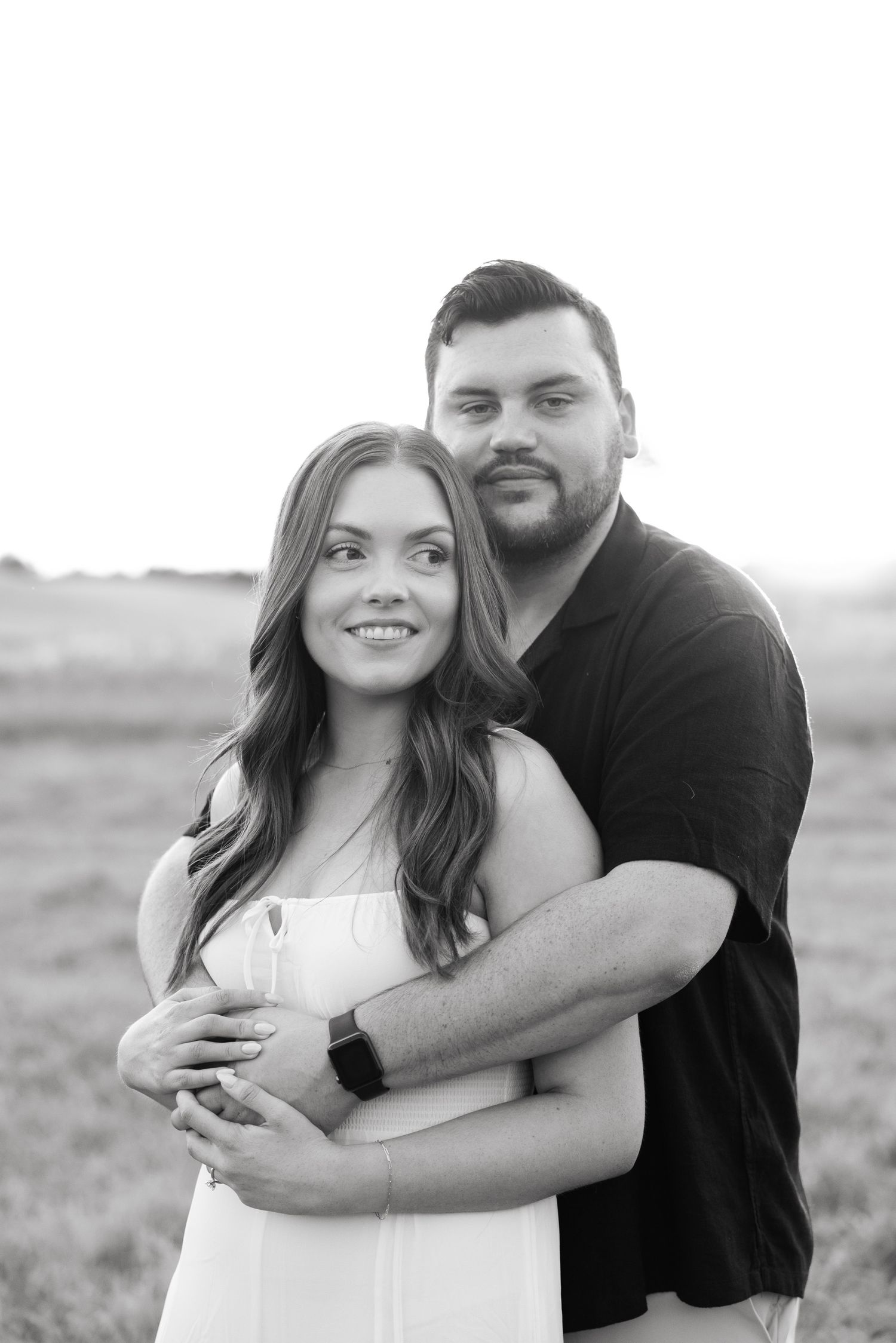 Black and white portrait of embracing couple in casual attire outdoors.