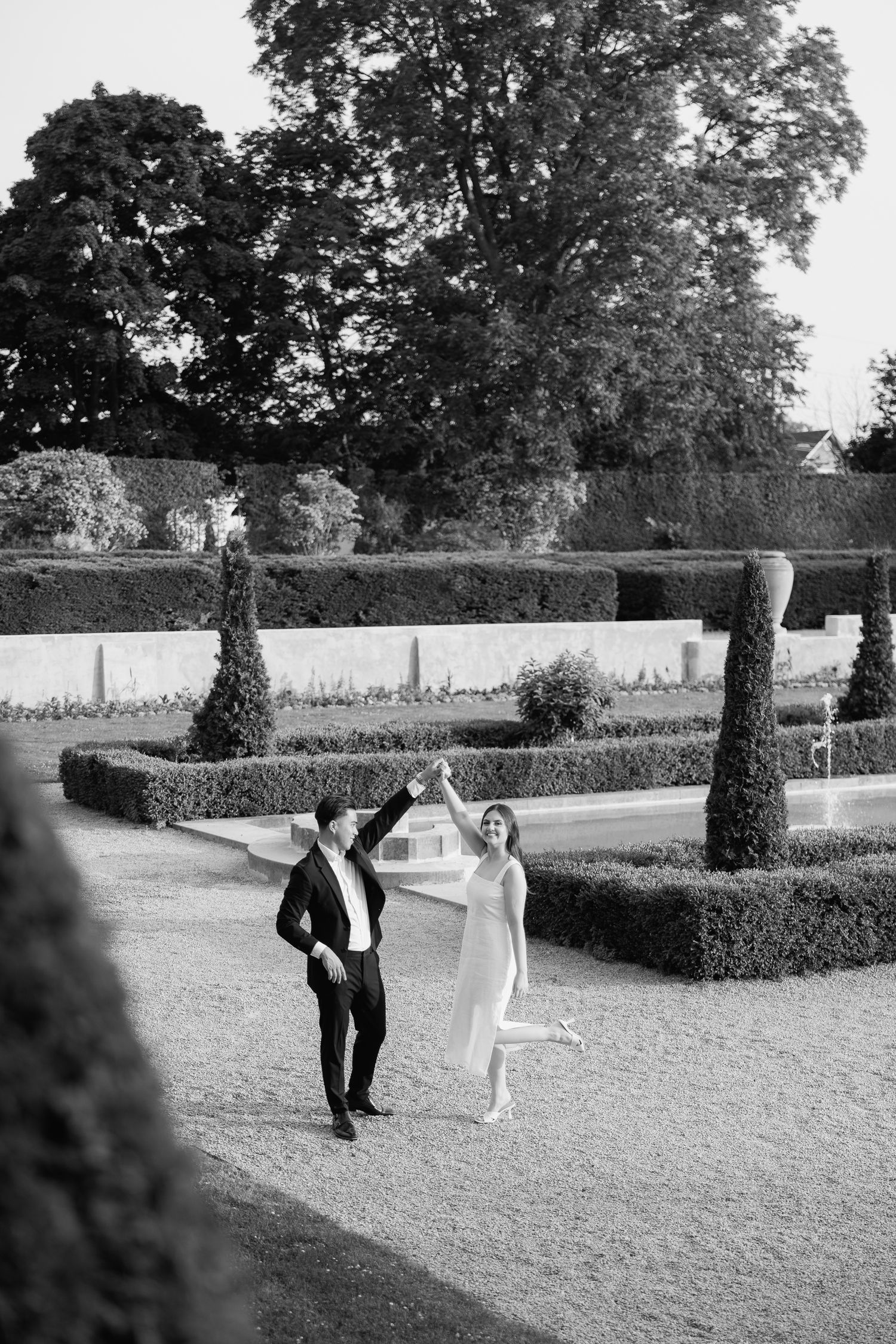 A couple joyfully walking together in a formal garden with cypress trees and hedges.