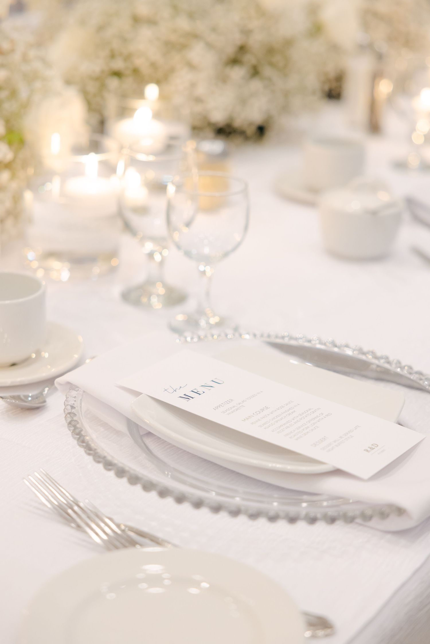 Formal place setting with beaded charger plate, menu card, and soft candlelight at elegant wedding reception.