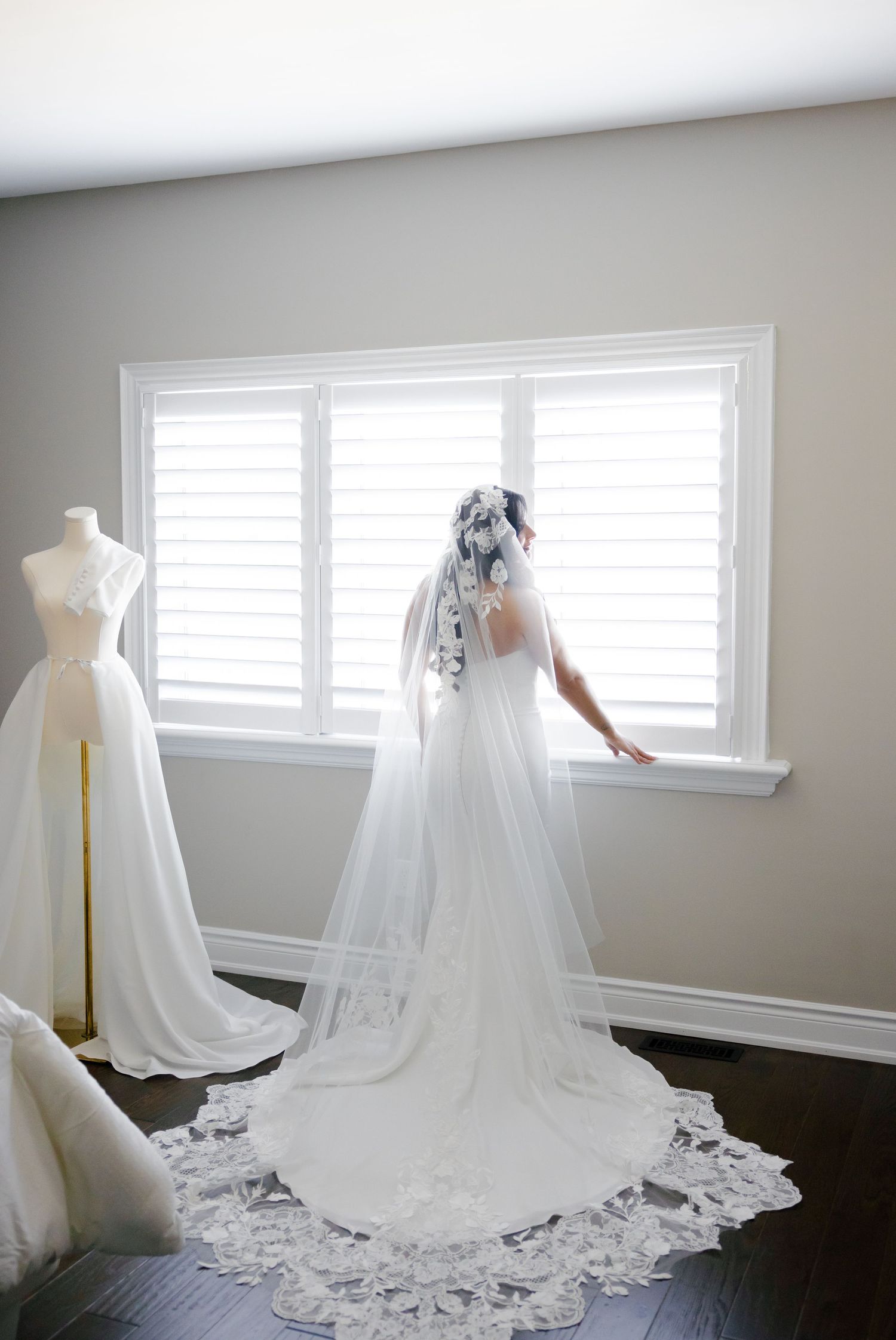 Wedding dress silhouette against bright windows with flowing lace-trimmed cathedral veil.