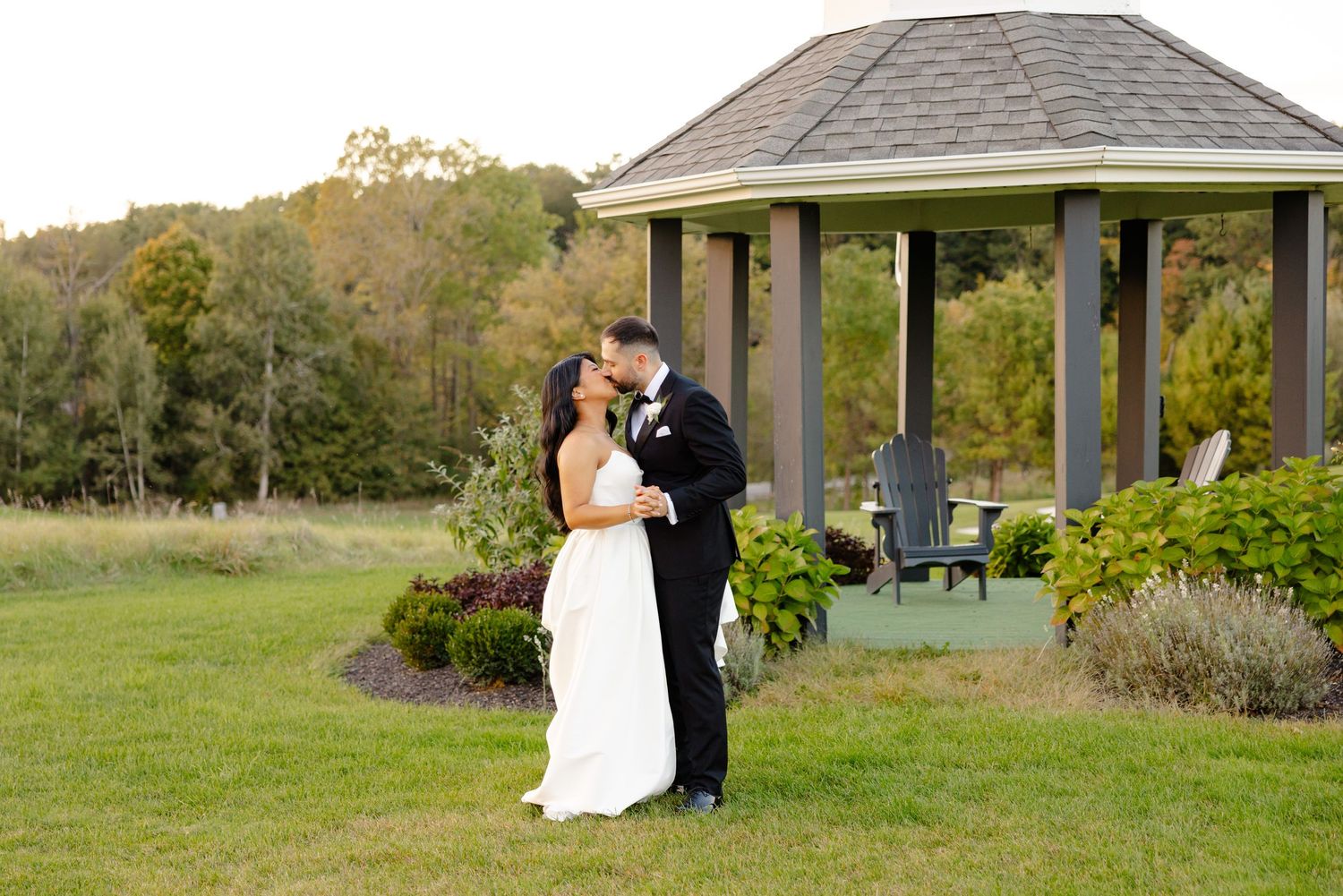 Elegant couple embracing near a garden gazebo during an outdoor wedding celebration.