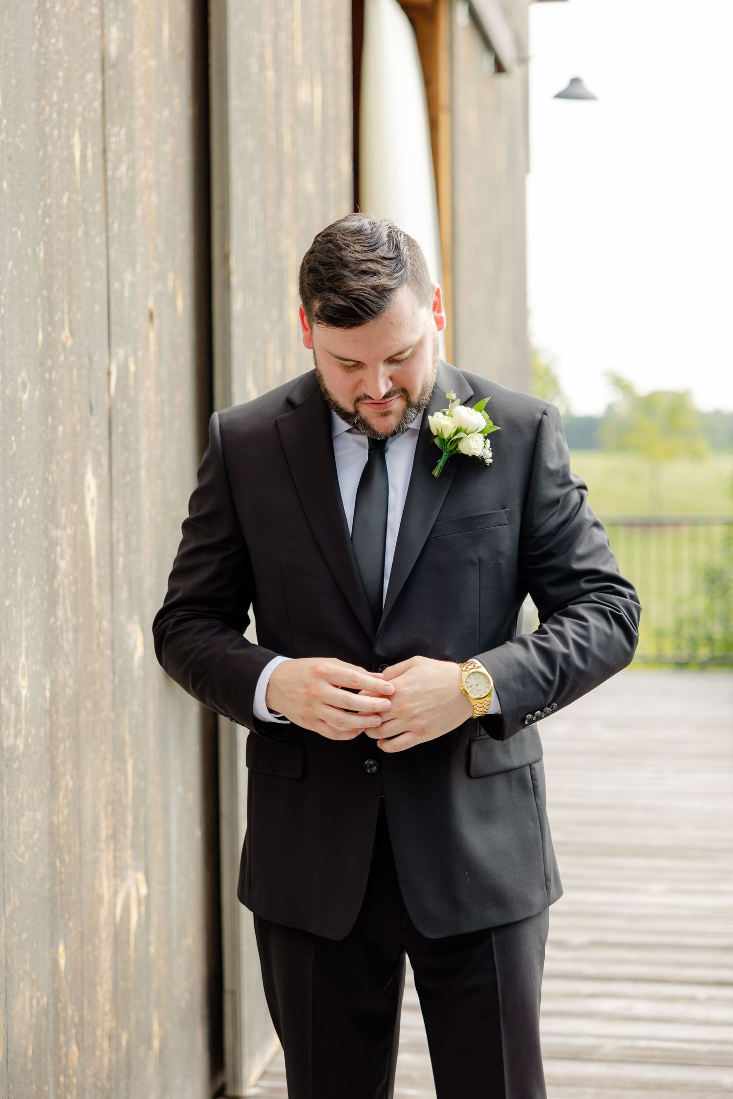 Person in formal black suit adjusts clothing while standing on outdoor deck.