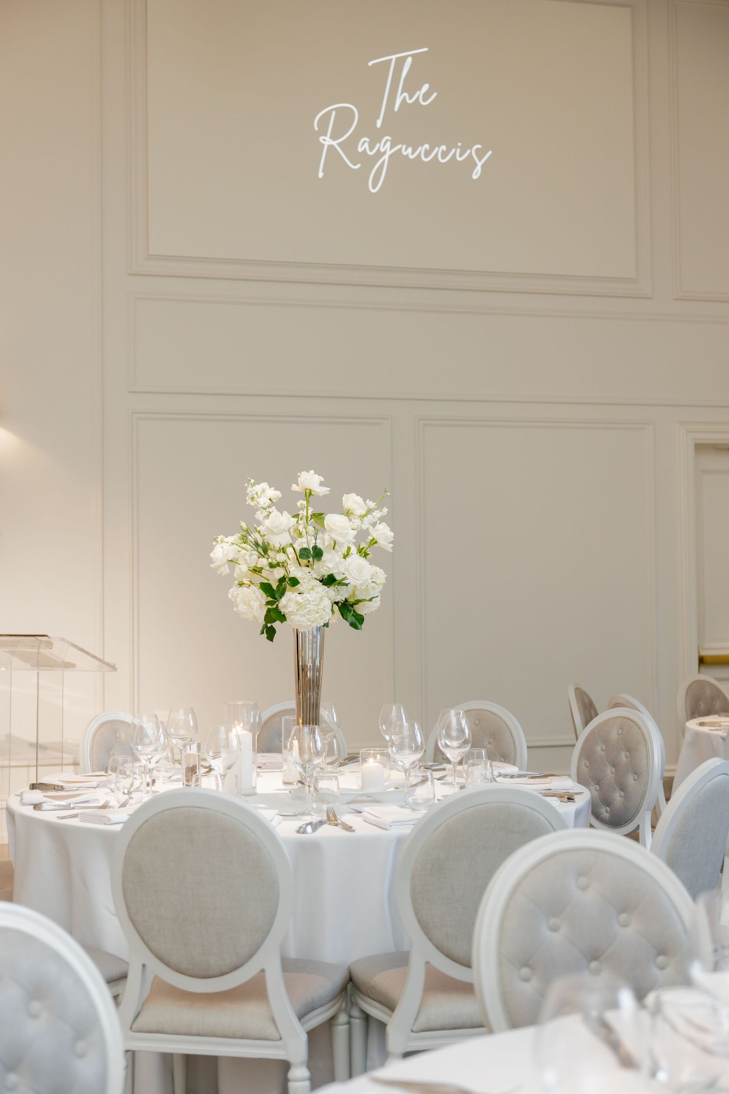 Elegant wedding reception table with white floral arrangement under cursive wall signage.