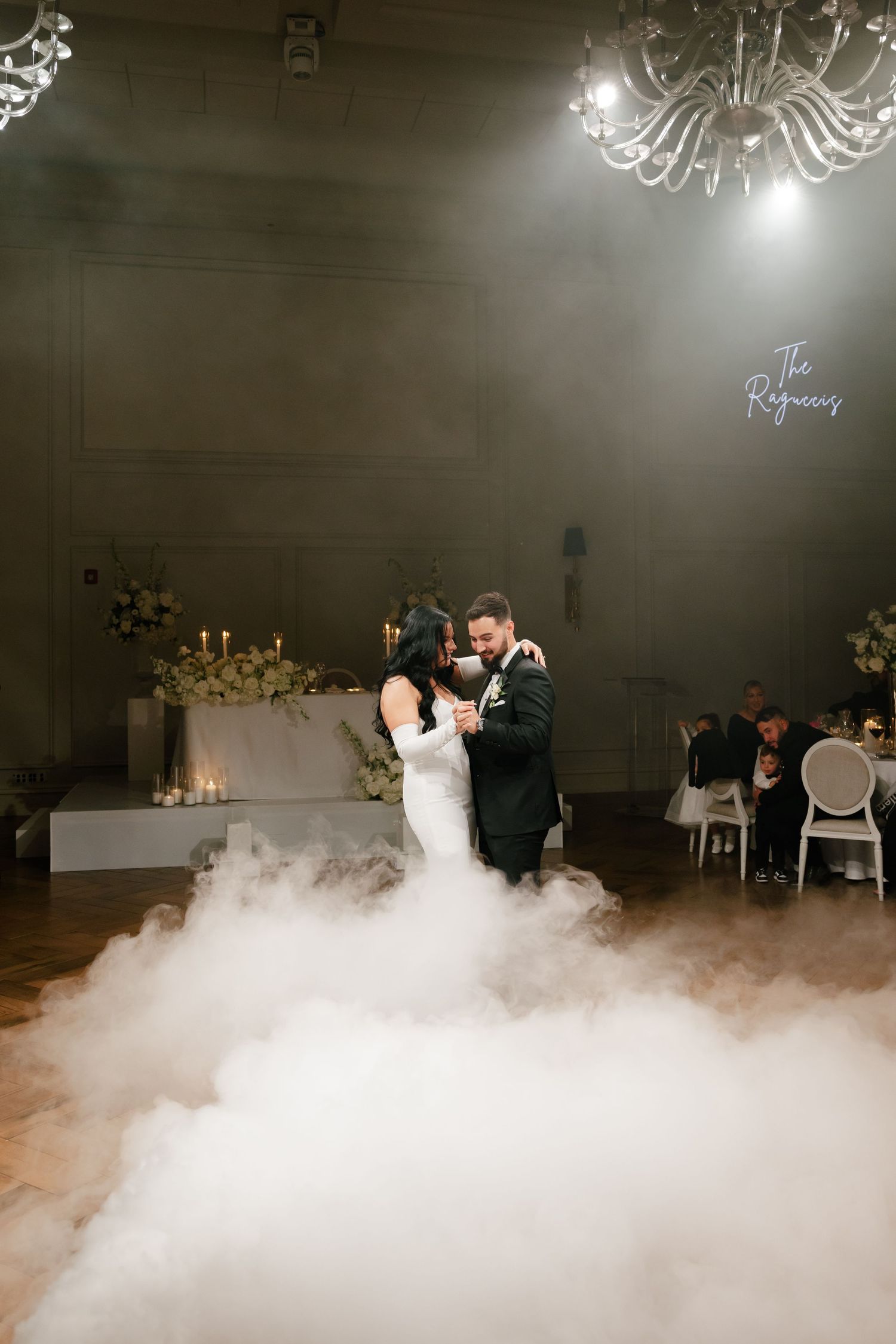 Couple's first dance surrounded by fog effects and romantic lighting at wedding reception.
