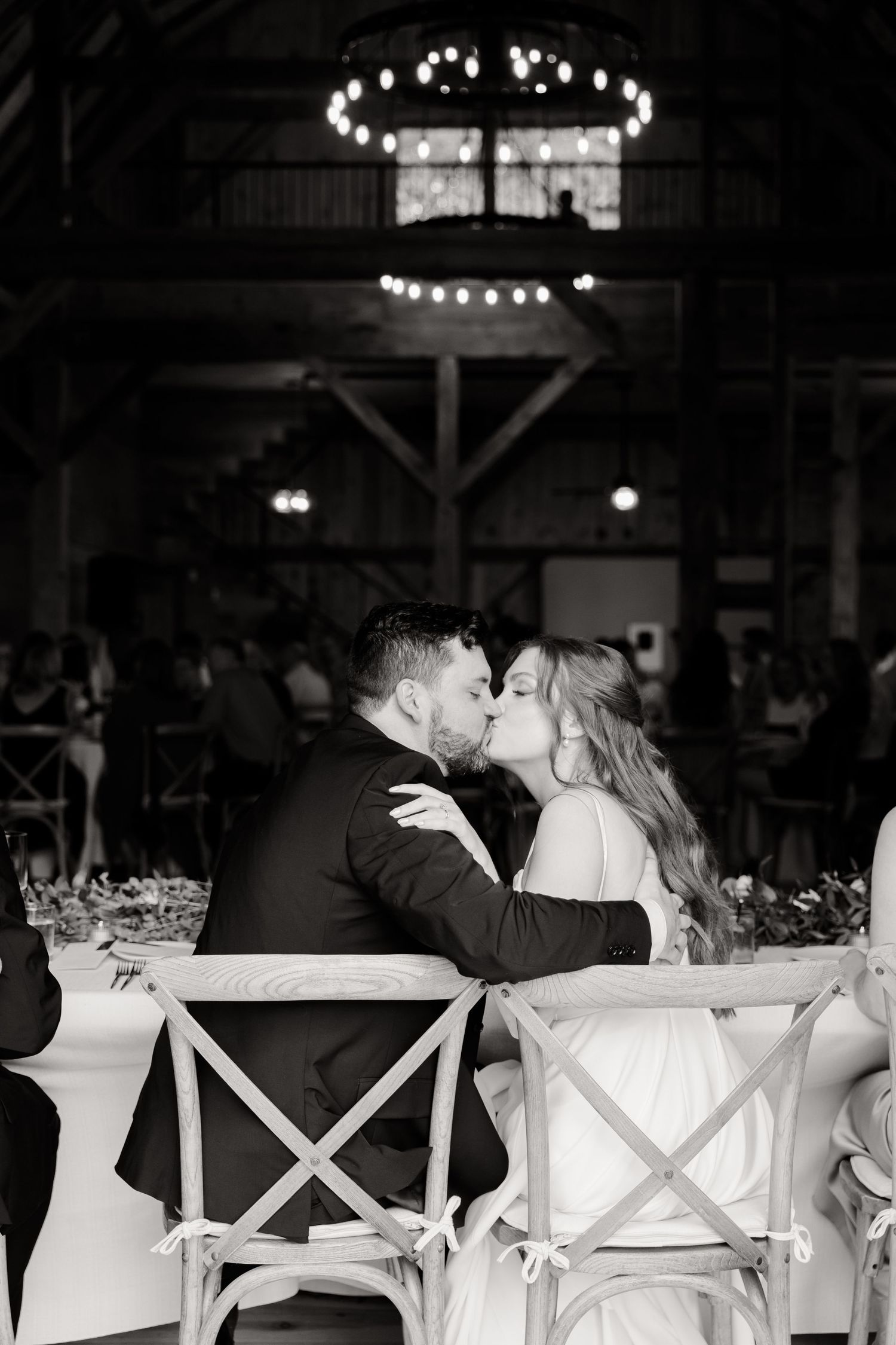 Black and white photo of a romantic moment during a barn wedding reception under twinkling lights.