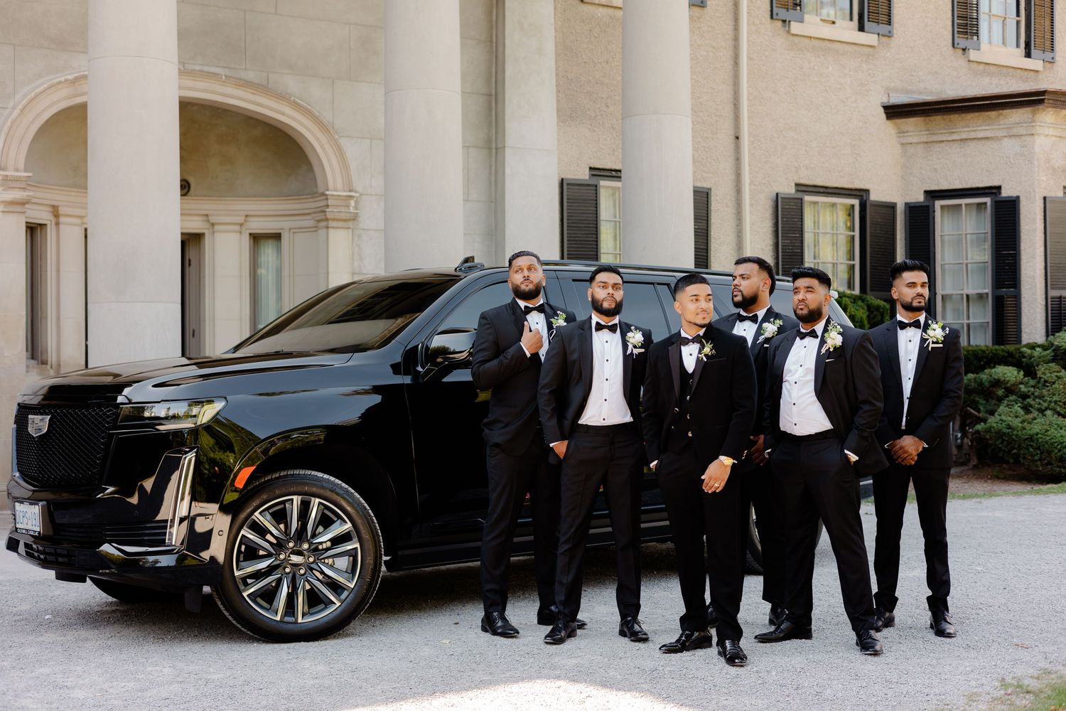 Black and white photo of groomsmen posing confidently next to a luxury vehicle.