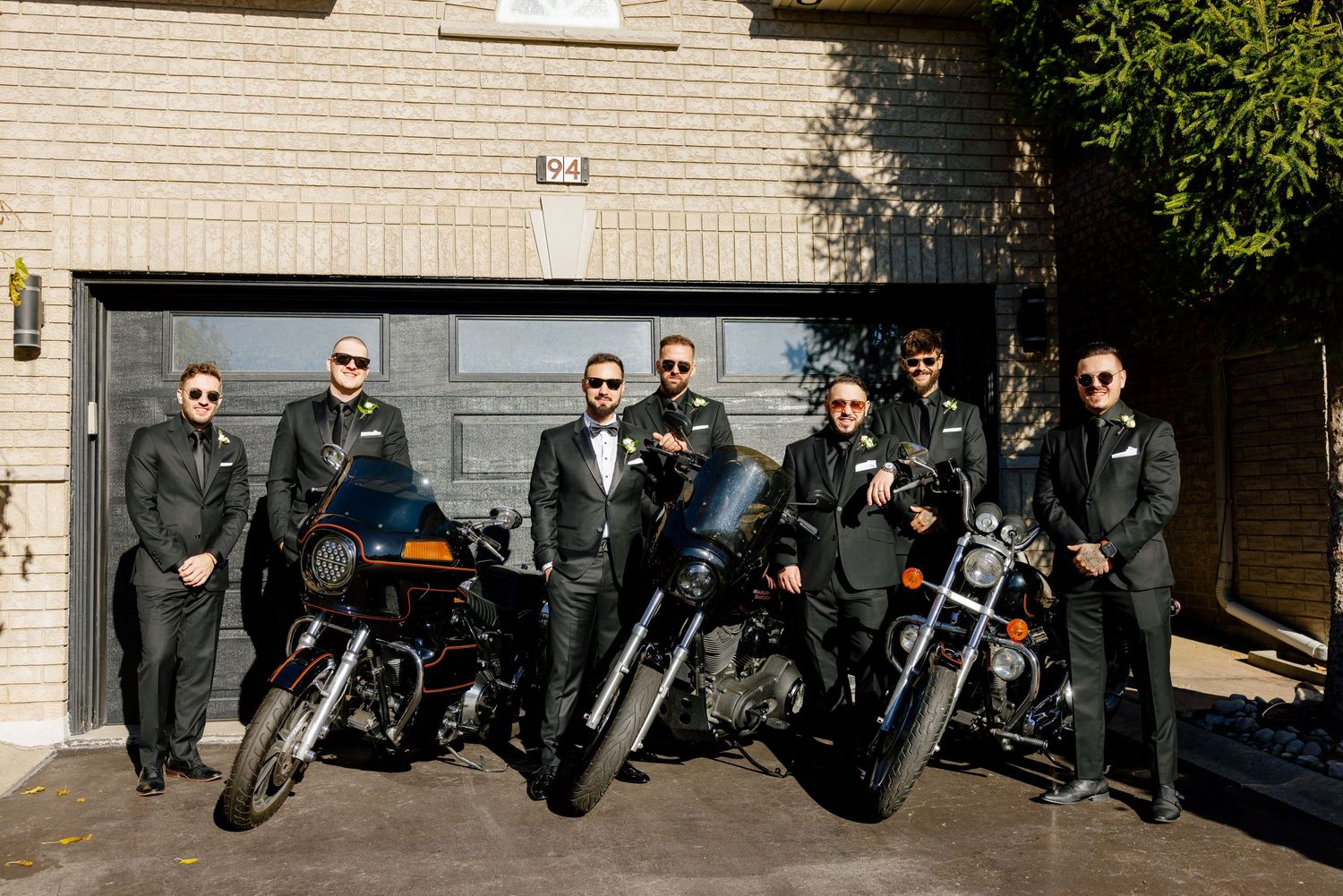 Motorcycle enthusiasts line up their bikes for a group photo against a brick wall.