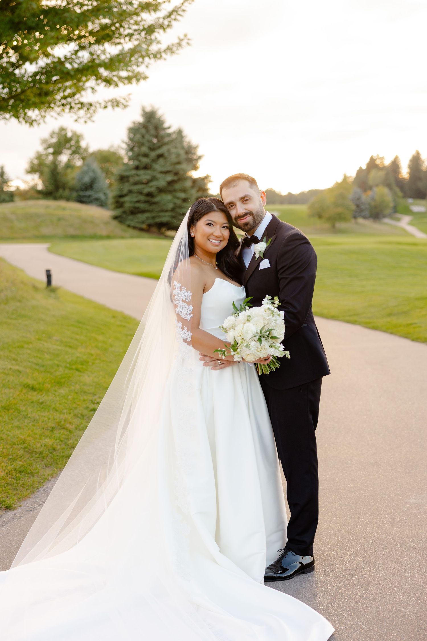 A tender moment between newlyweds on a golf course path with white bouquet.