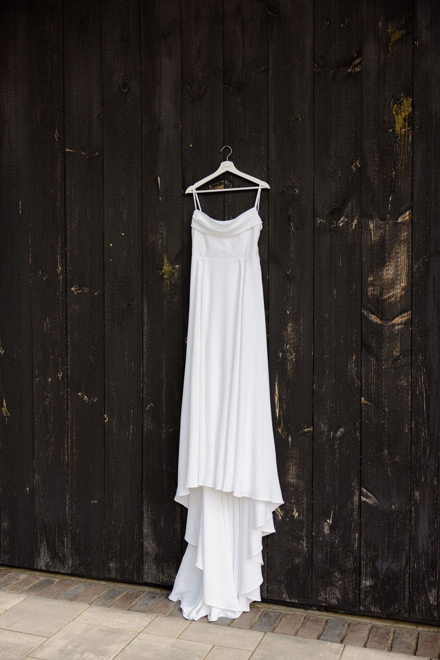 White wedding dress hanging on wooden wall creating dramatic contrast.