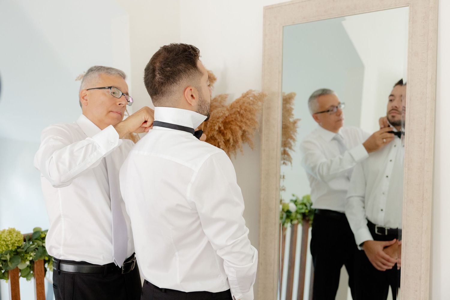 Two people in white shirts making final adjustments in front of mirror.