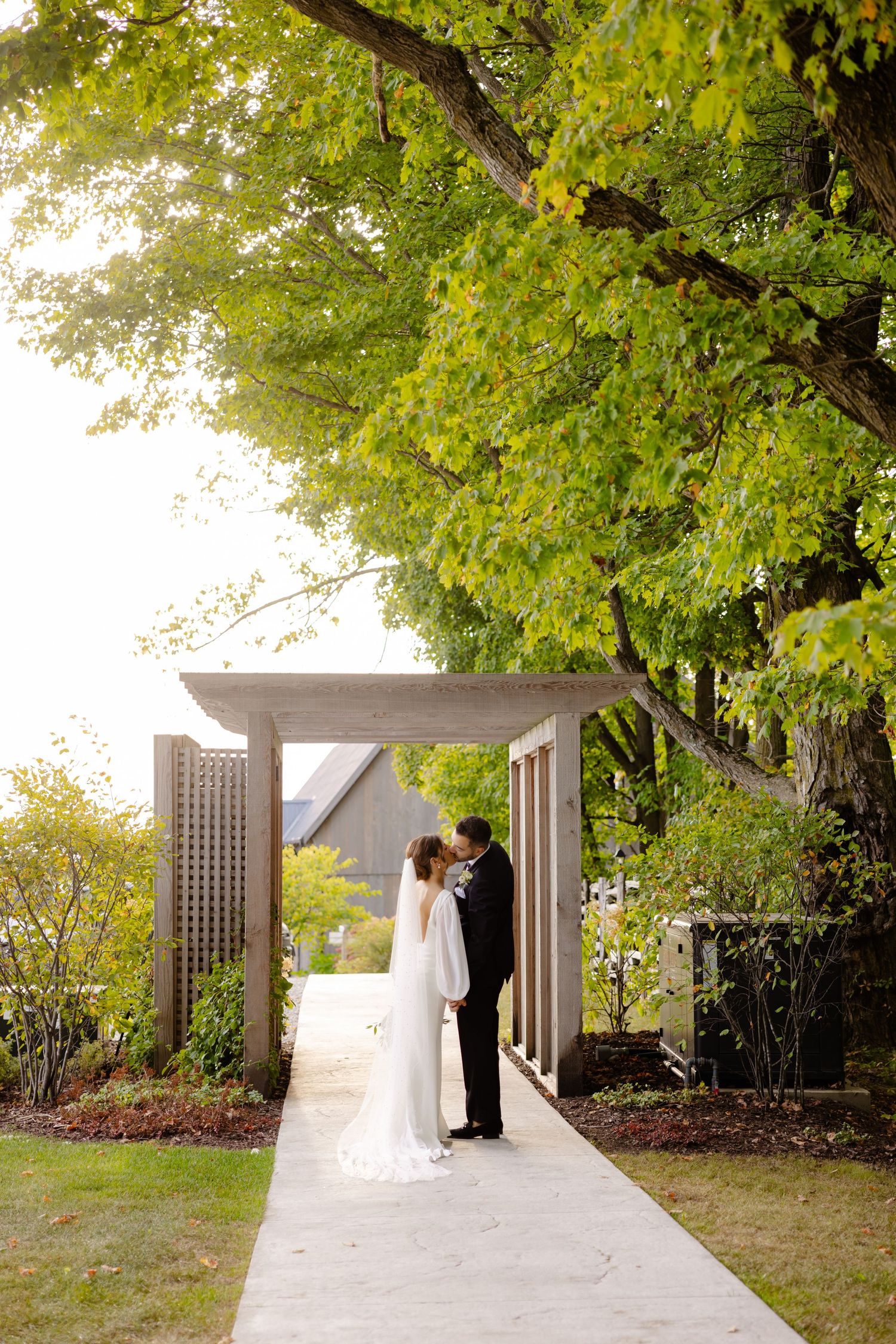 Intimate wedding moment captured under an arbor surrounded by lush green trees.