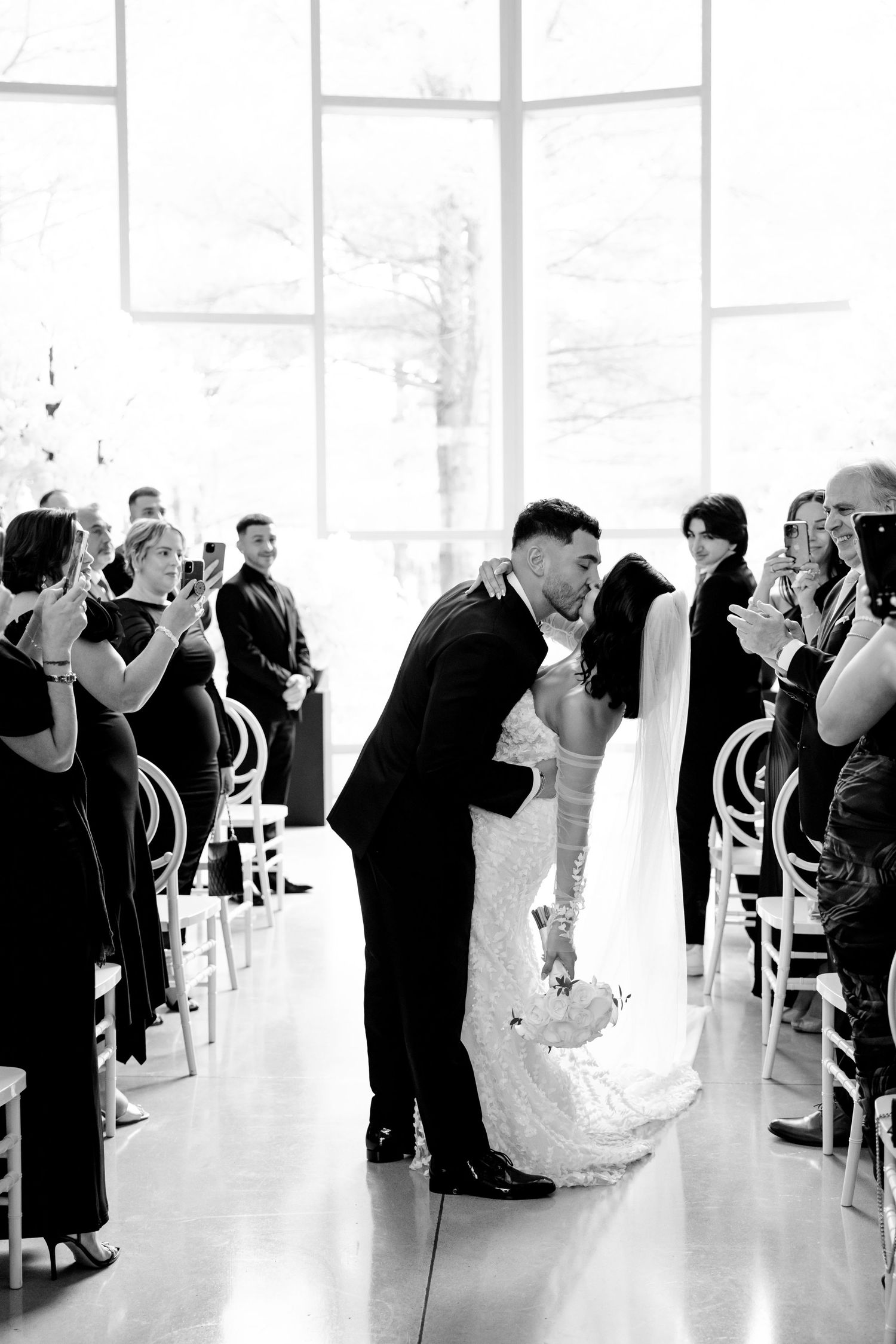 A black and white wedding ceremony photo with guests applauding in an elegant venue.