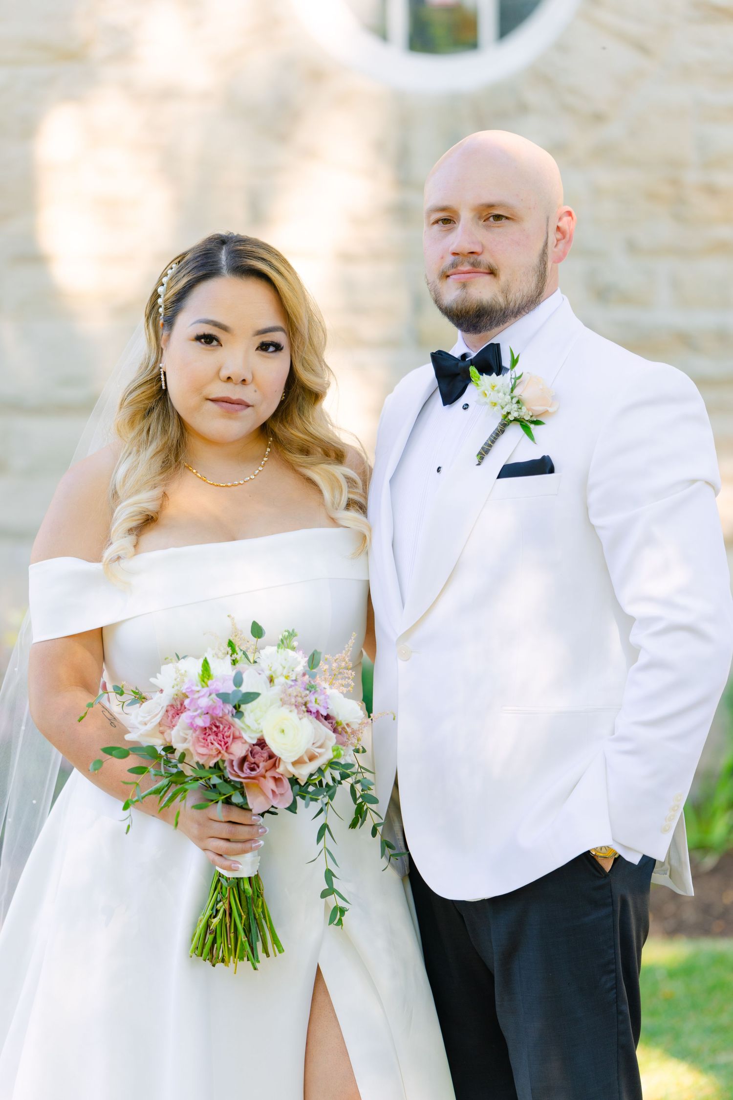 Couple in white formal wedding attire poses with pink and green floral bouquet.