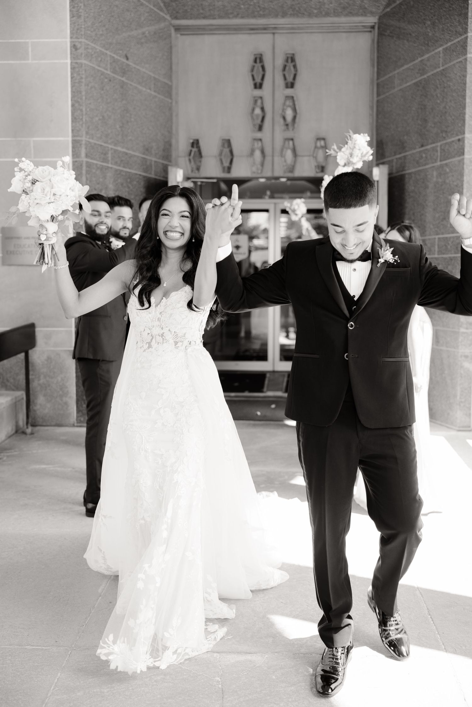 Black and white photo of newlyweds celebrating with raised arms during church exit.
