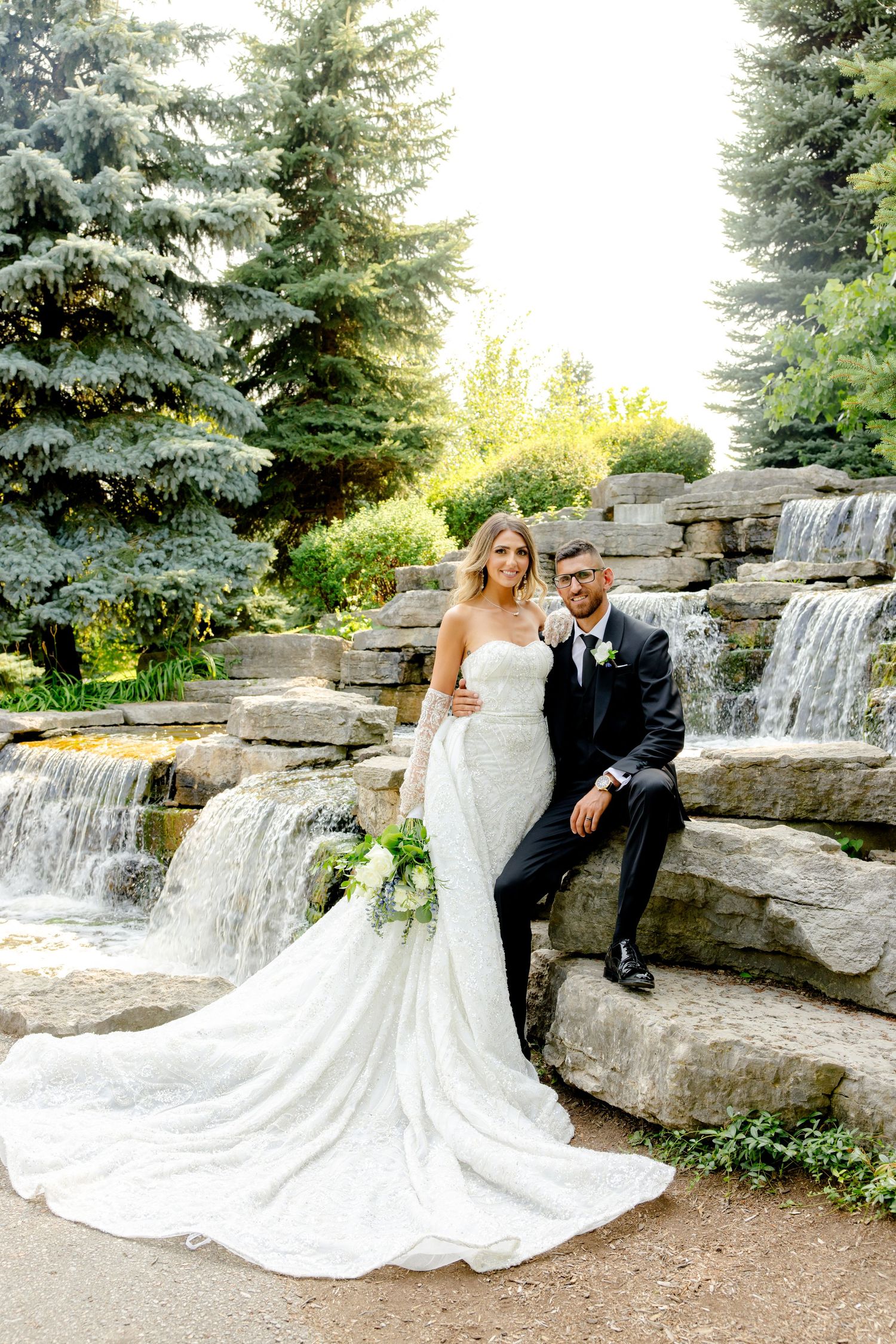 Elegant wedding photography of a couple posing on stone waterfall steps surrounded by evergreen trees.