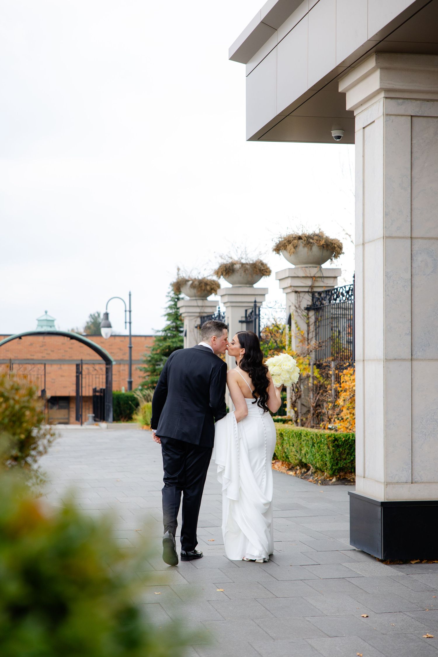 Wedding couple pause beneath decorative columns with floral arrangements overhead.