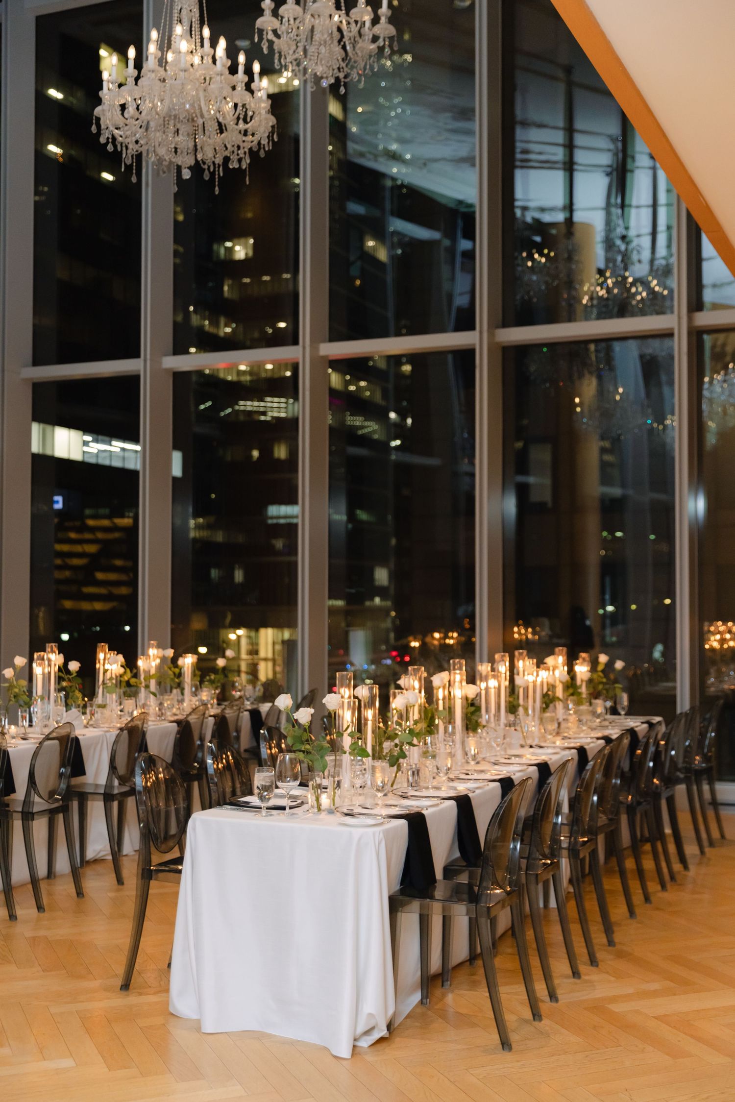 Formal dining setup with crystal chandeliers and floor-to-ceiling windows overlooking city lights.