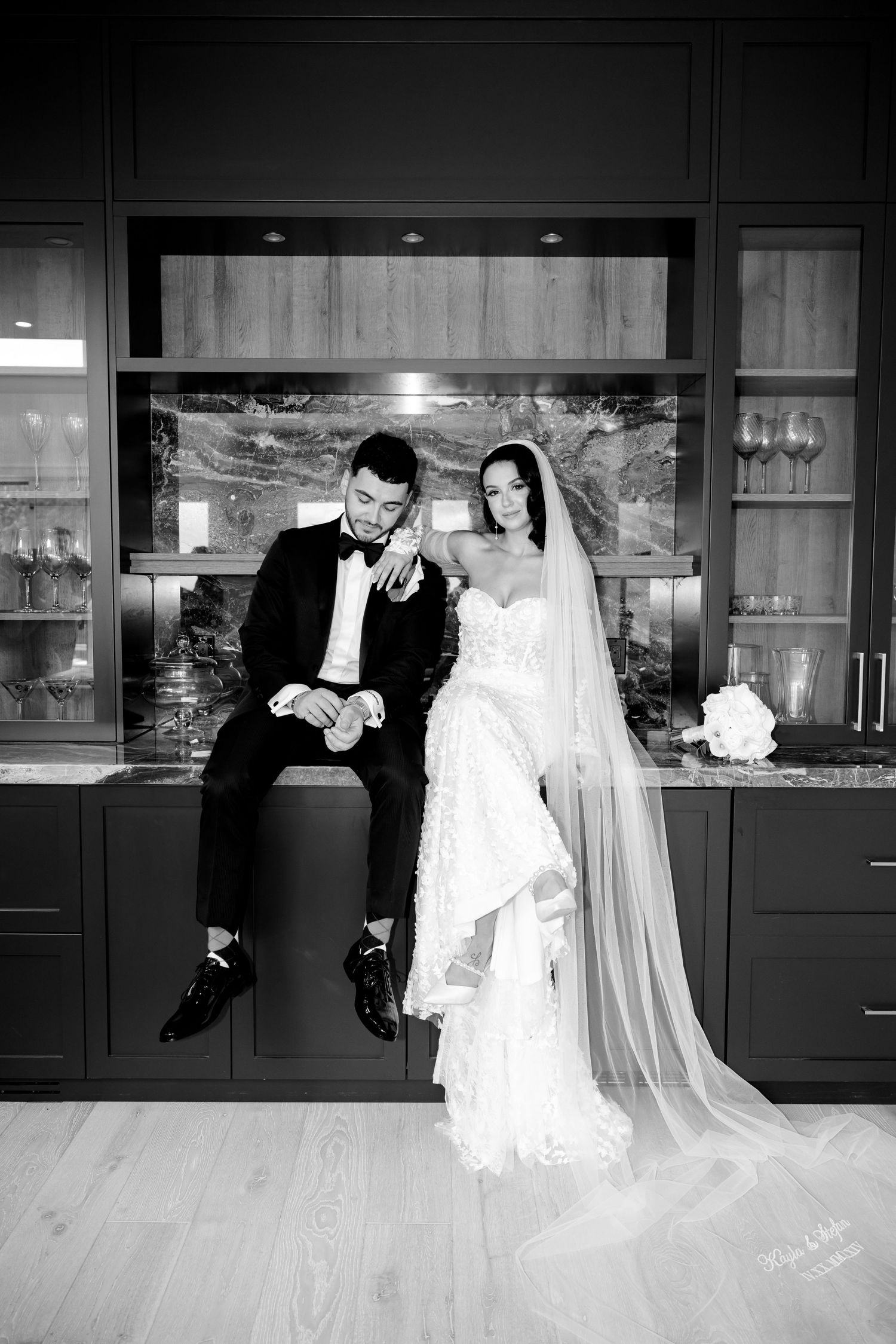 An intimate wedding portrait showing a couple in formal attire against dark kitchen cabinets.
