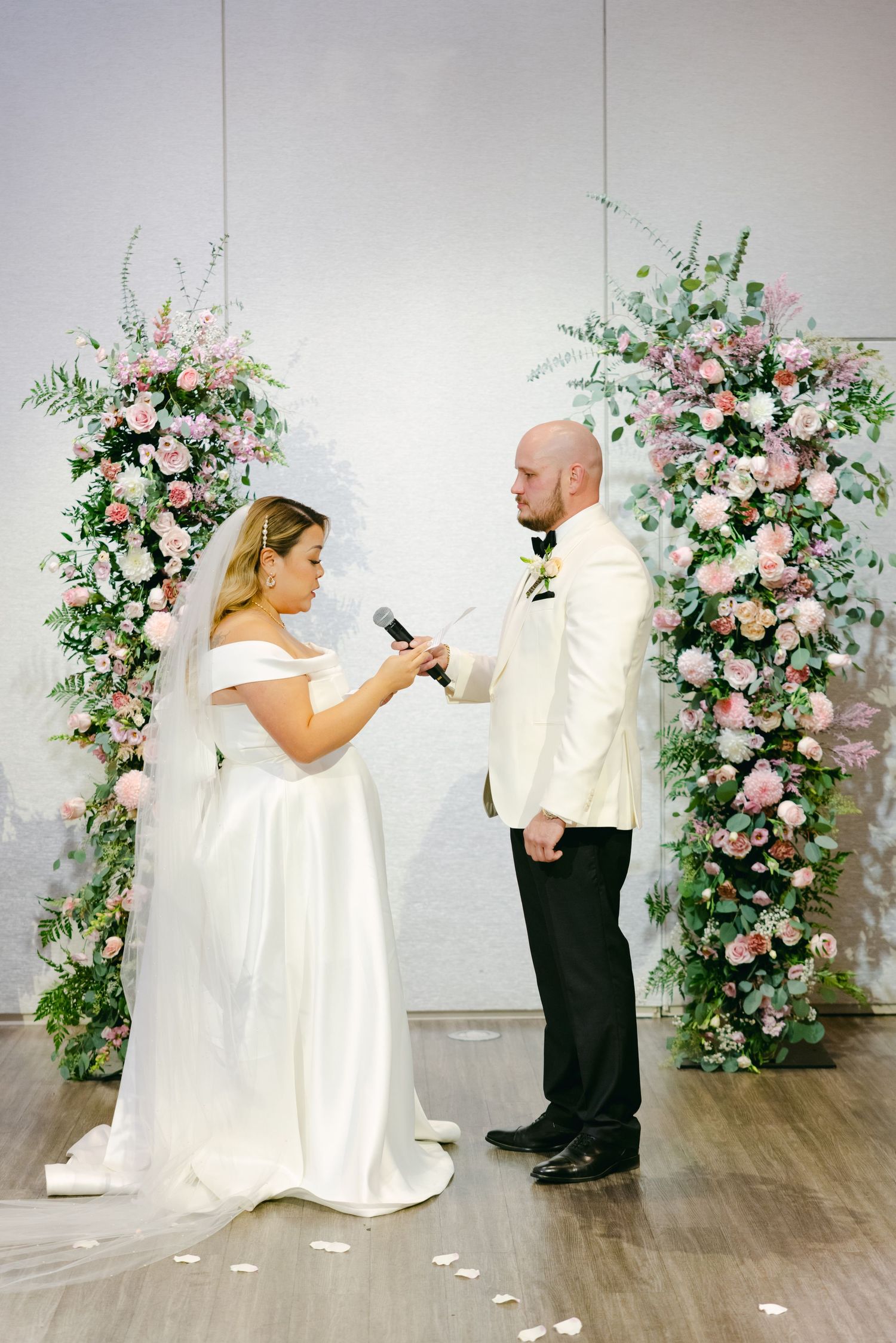 Couple exchanging vows between pink and white floral arrangements during ceremony.