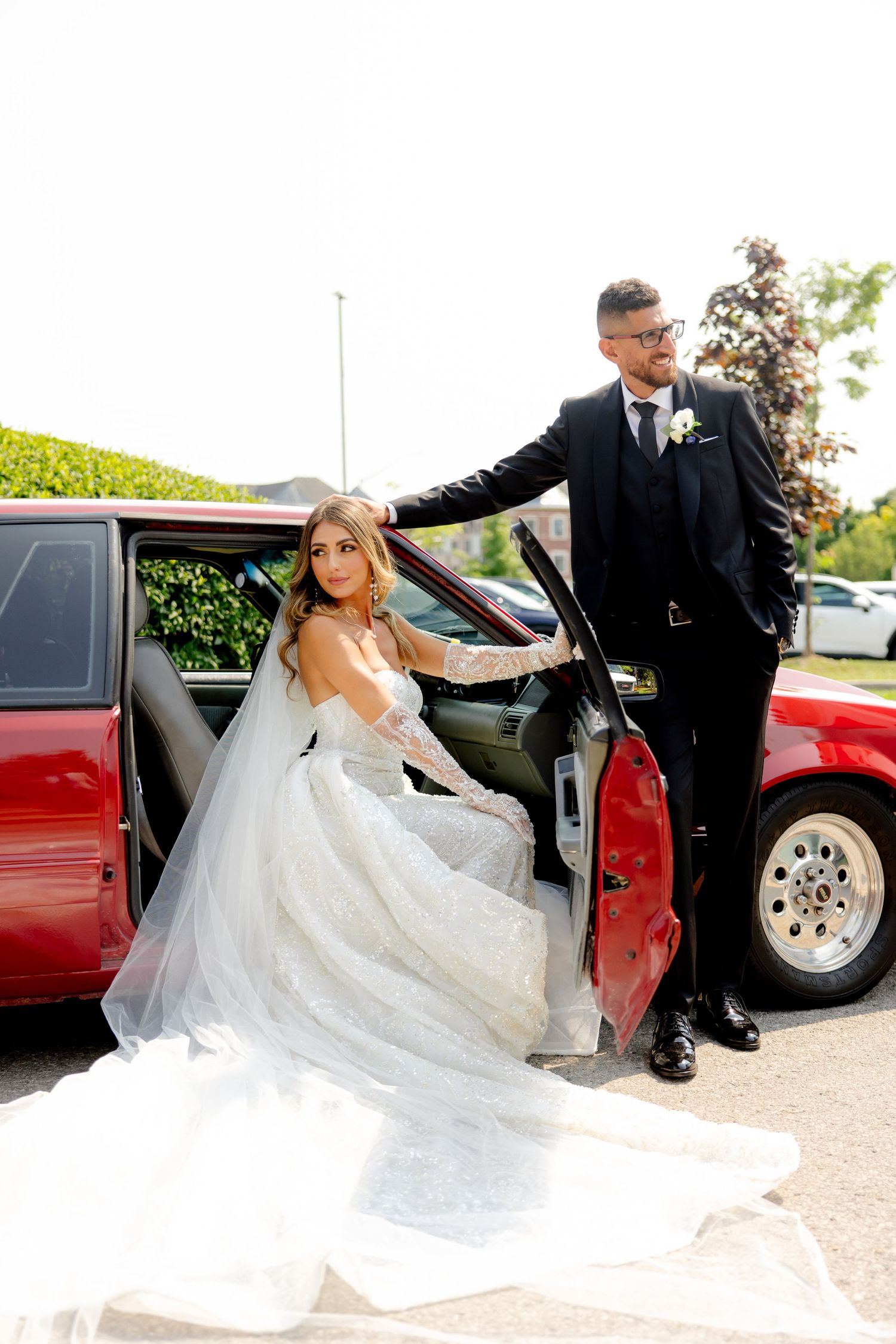 Wedding photo featuring a red car while the bride gracefully exits the vehicle.