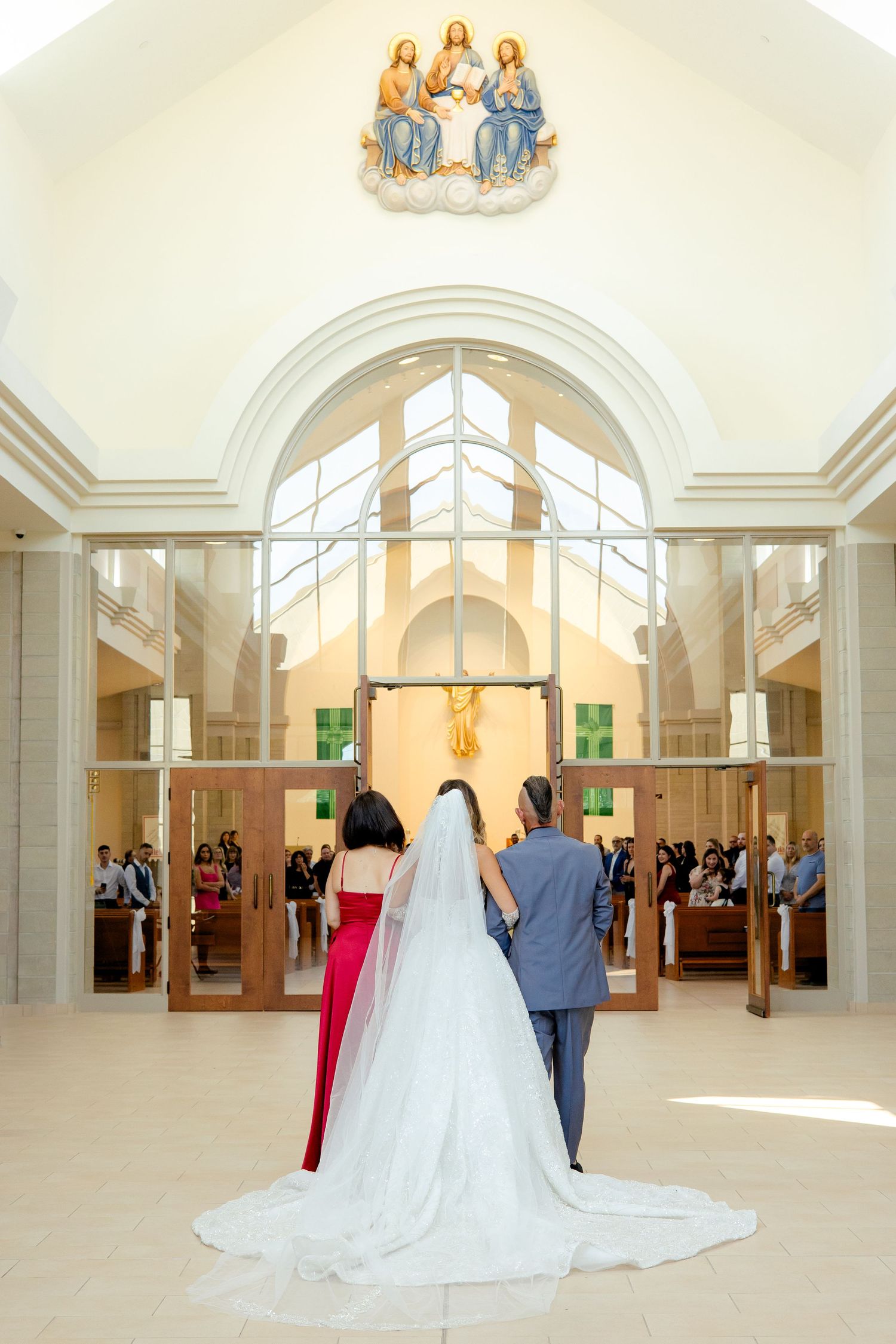 A wedding ceremony in a bright modern church with an arched ceiling and religious artwork visible above.