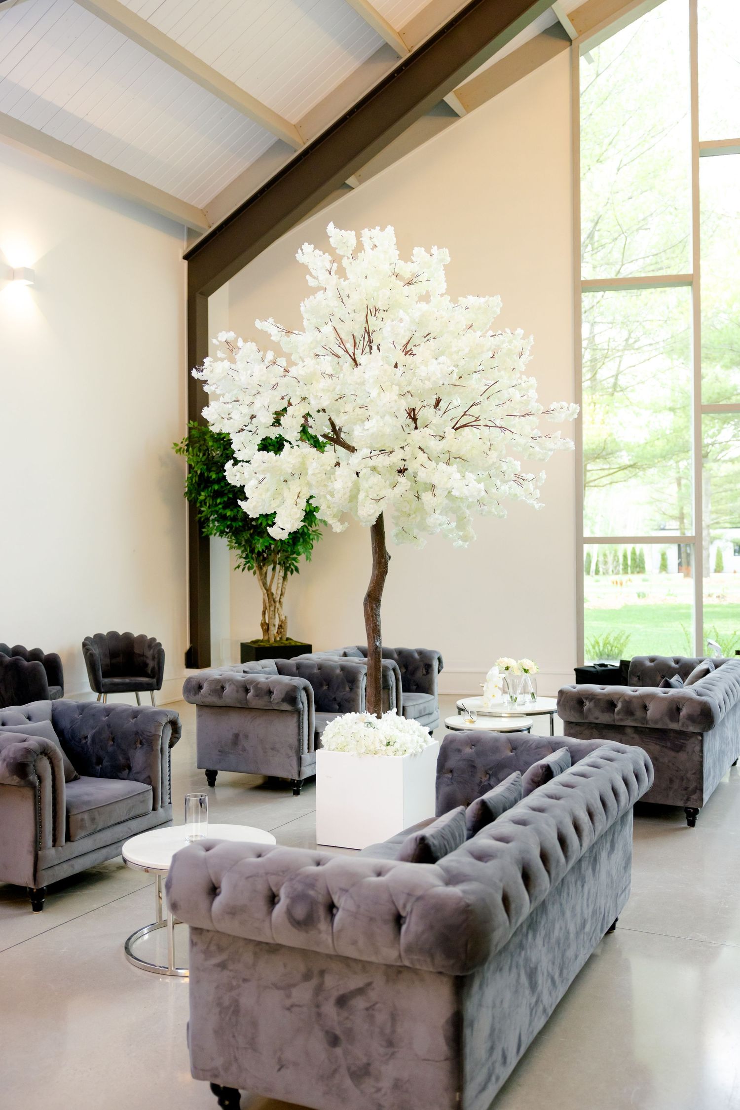 A luxurious lounge area with grey tufted furniture and a white floral tree centerpiece.