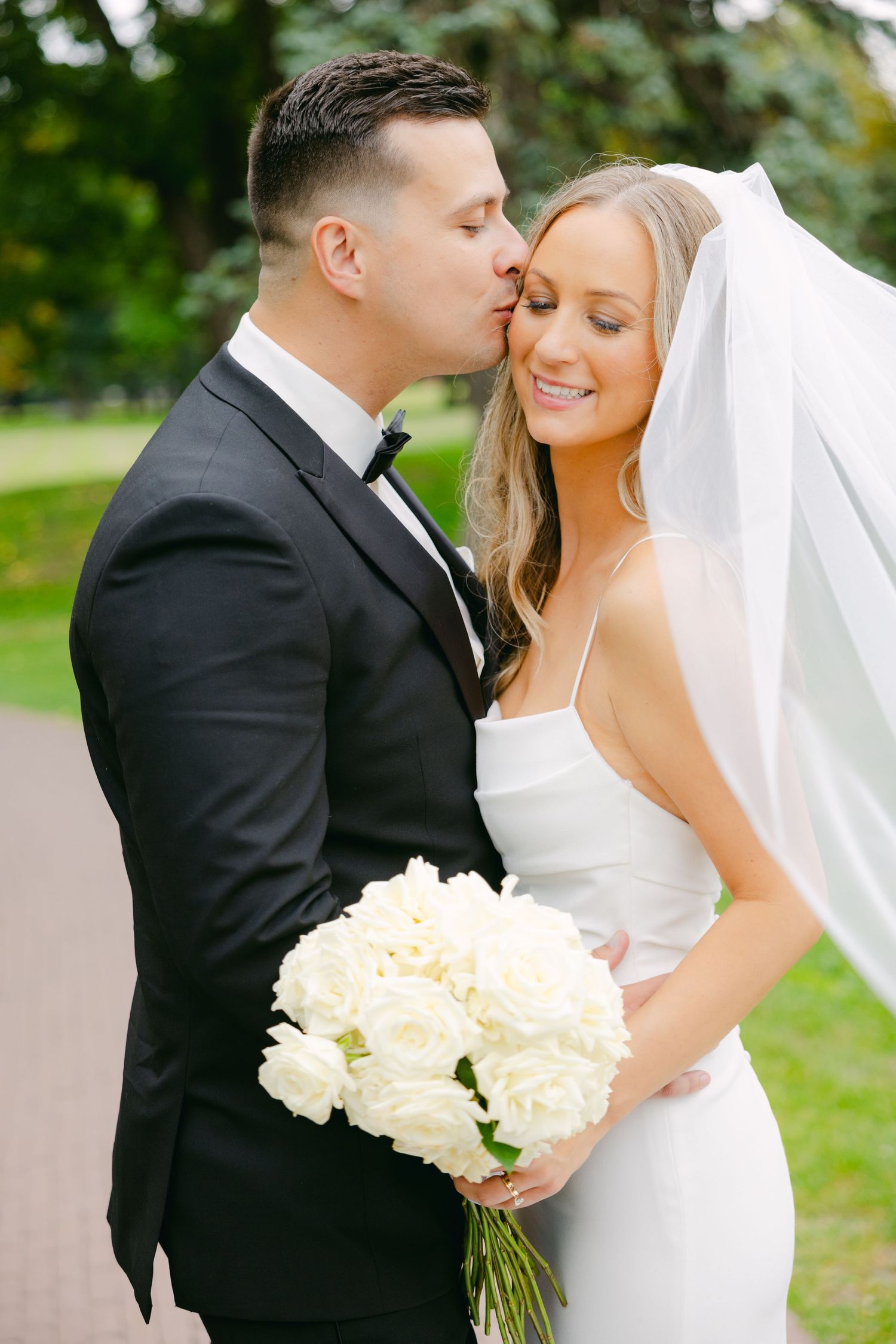 Intimate garden wedding portrait with white roses and flowing veil.