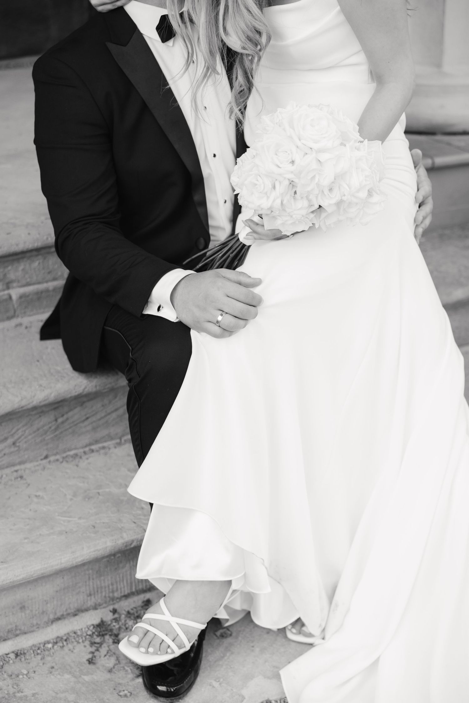Detail shot of wedding couple on stairs showing formal attire and bridal bouquet.