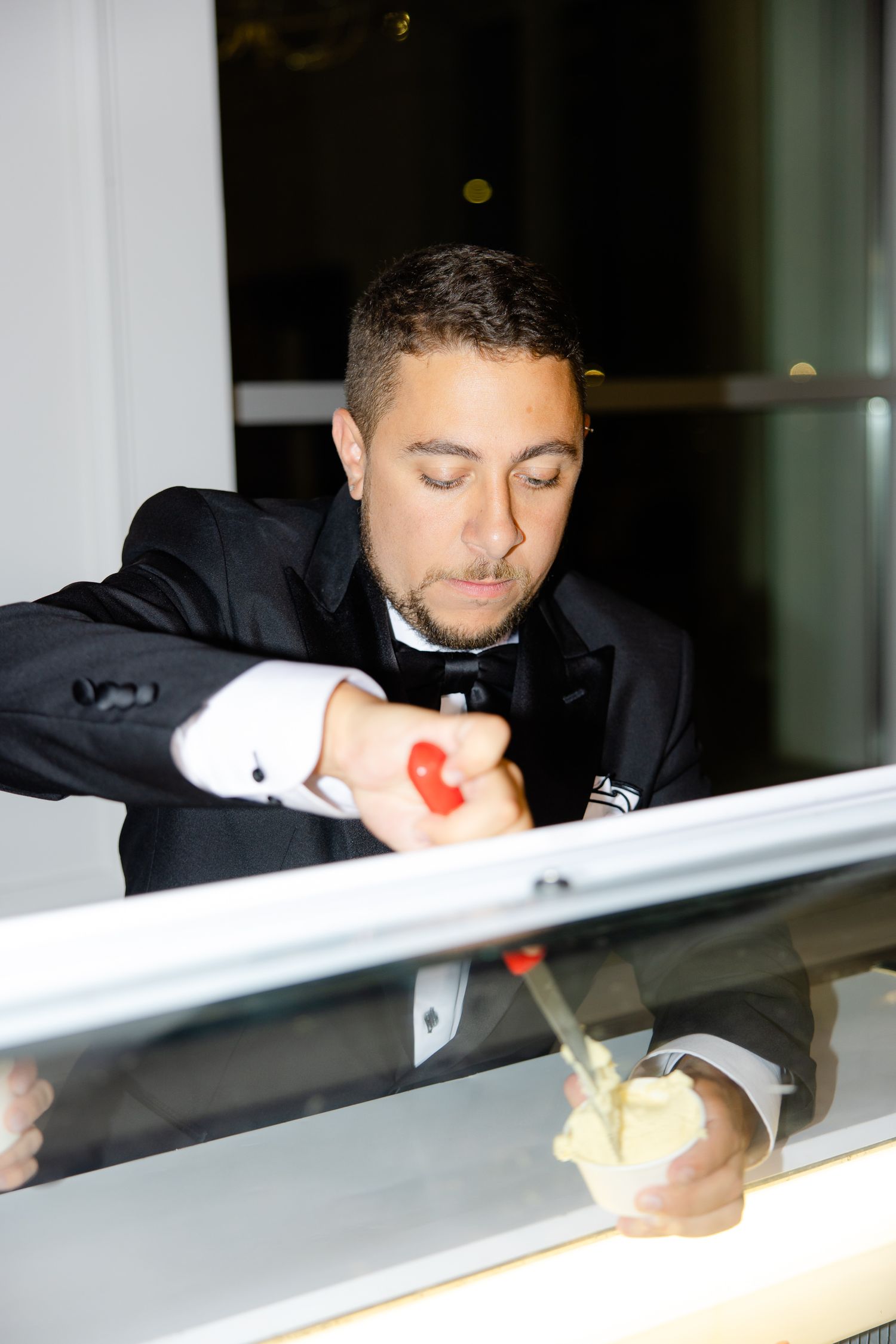Person in tuxedo scooping gelato from an elegant white display case.