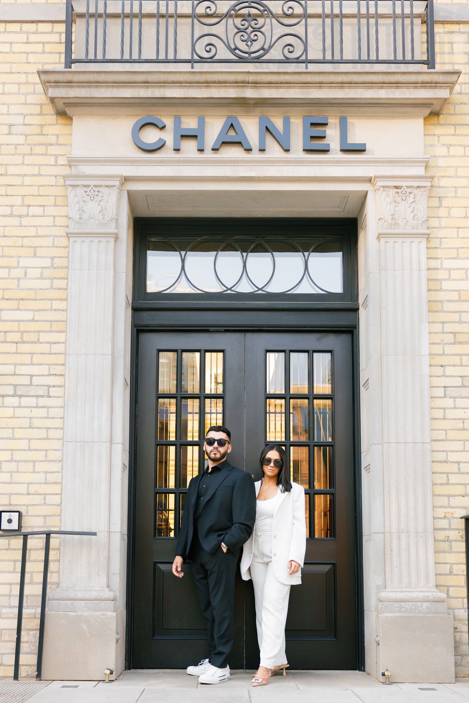 Fashion-forward couple poses in front of iconic Chanel storefront with classic architectural details.