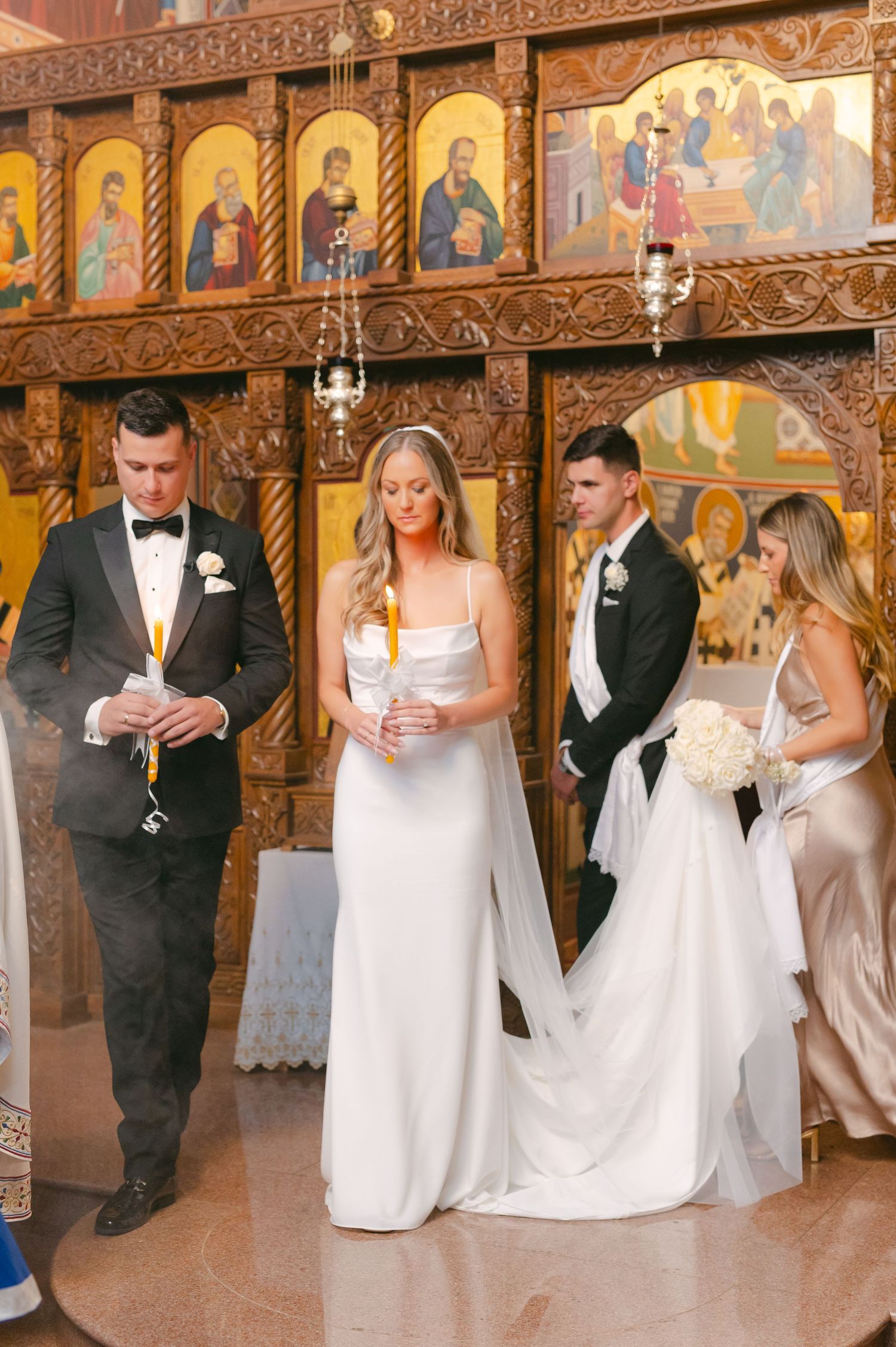 Wedding party standing before ornate religious iconography in Orthodox church.