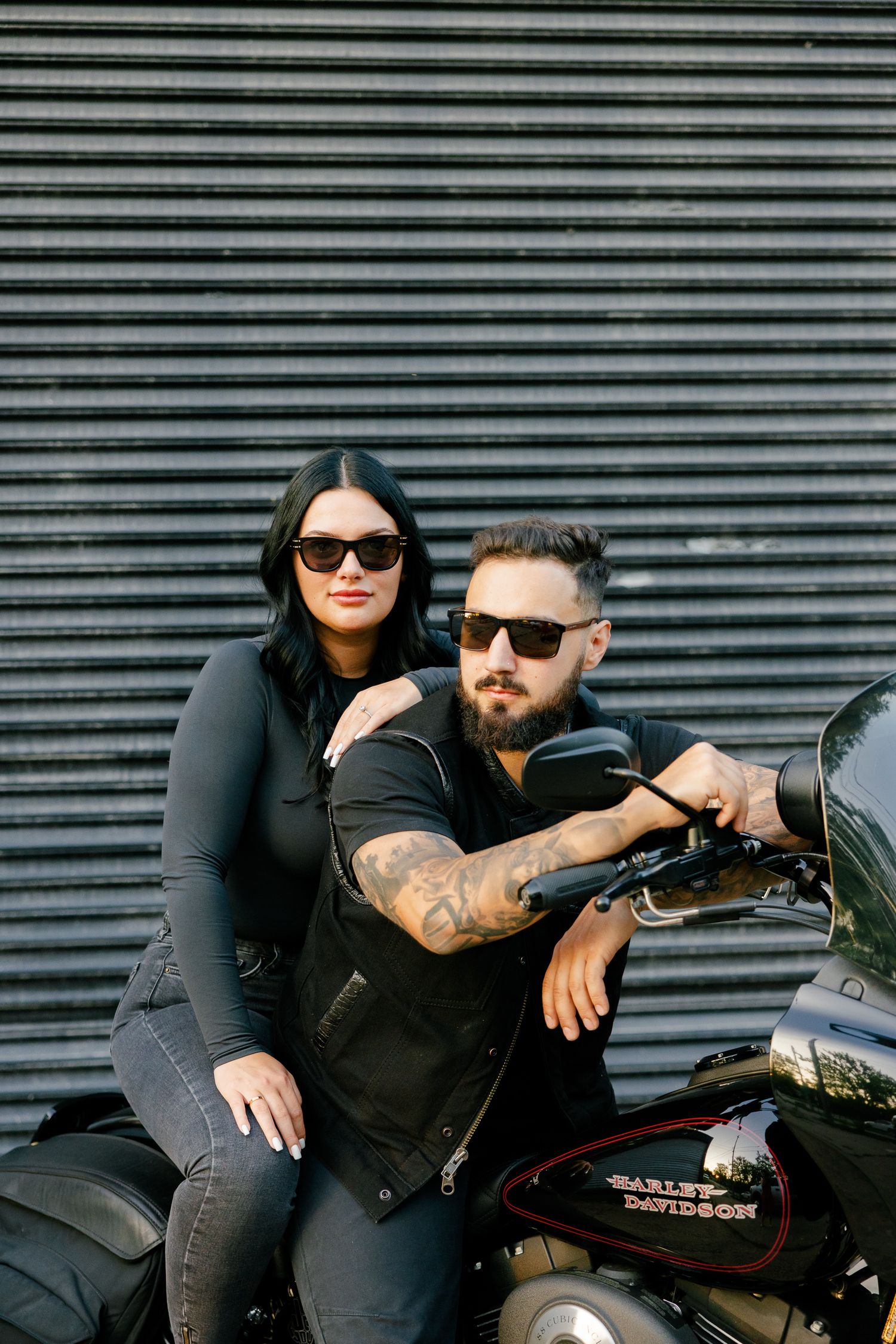Couple on motorcycle sharing intimate moment against industrial backdrop.