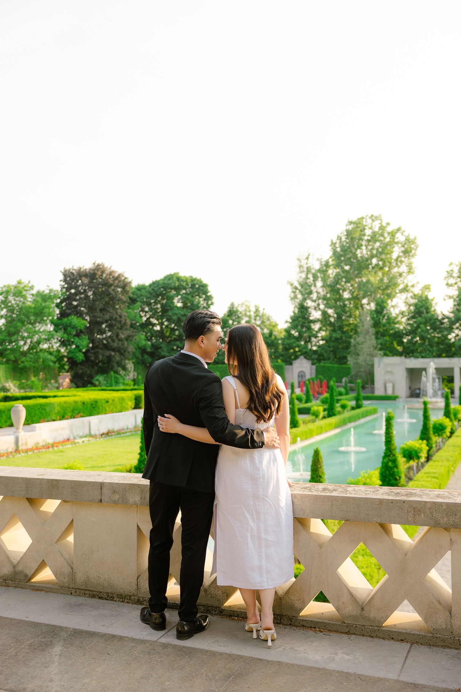 A couple admiring the view of formal gardens and fountains from an ornate balcony.