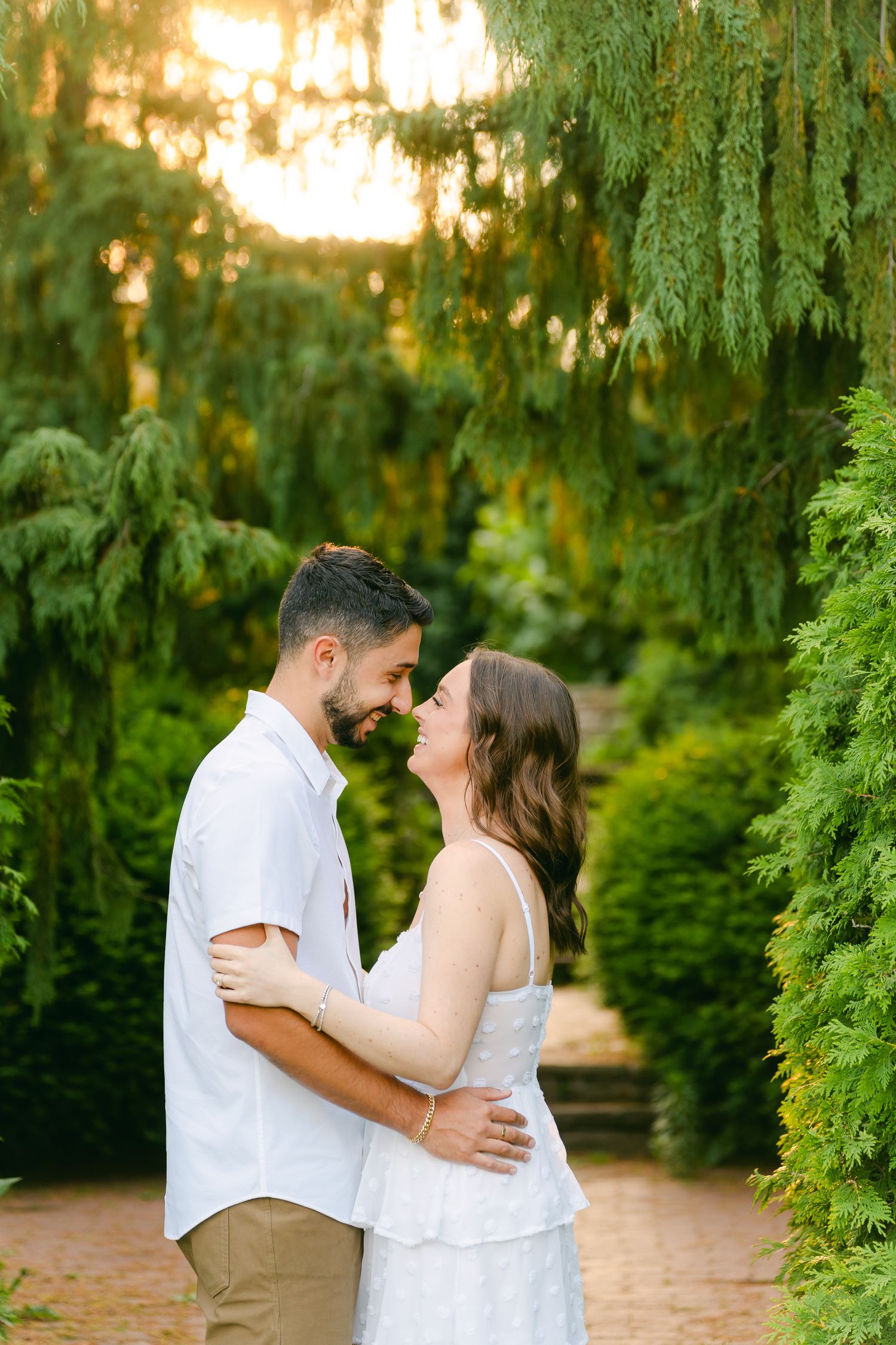 An intimate moment captured between a couple on a garden path surrounded by evergreen landscaping.