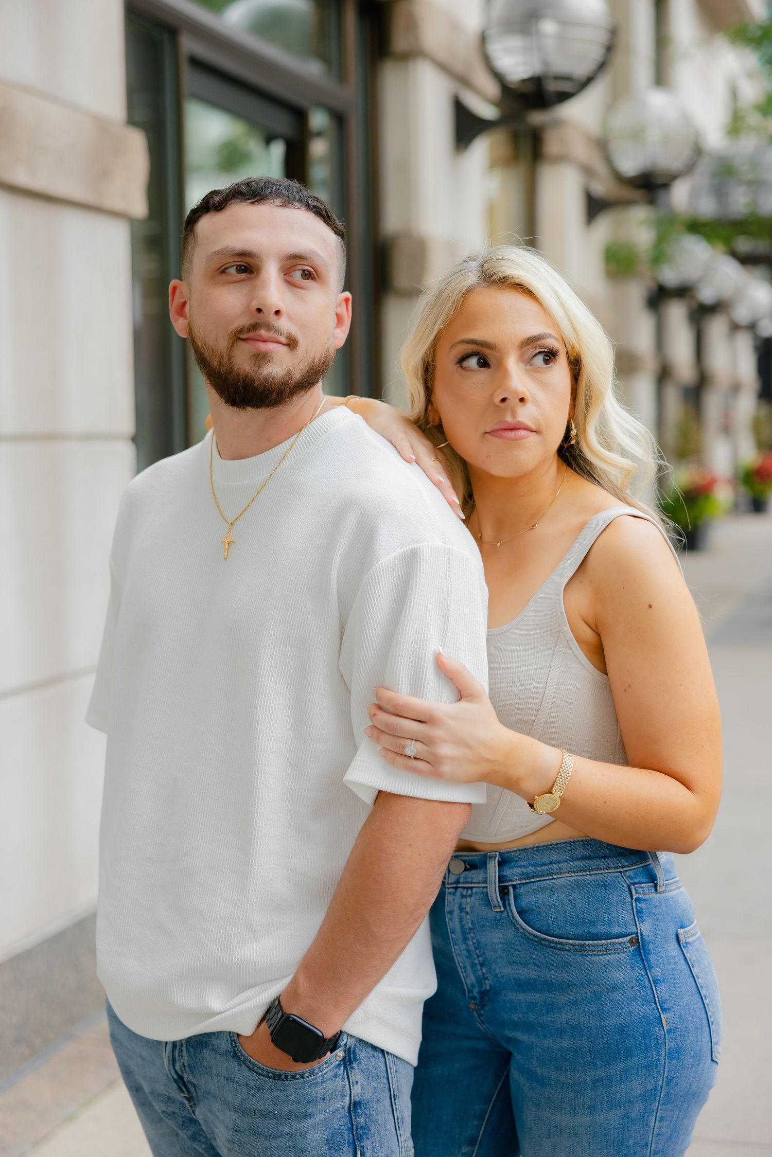 A couple in coordinated casual outfits posing against a building wall.