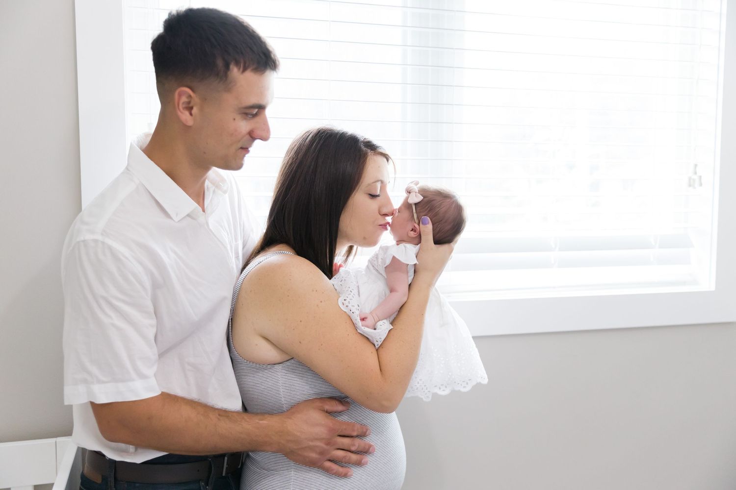 Family sharing tender moment with newborn by bright window.