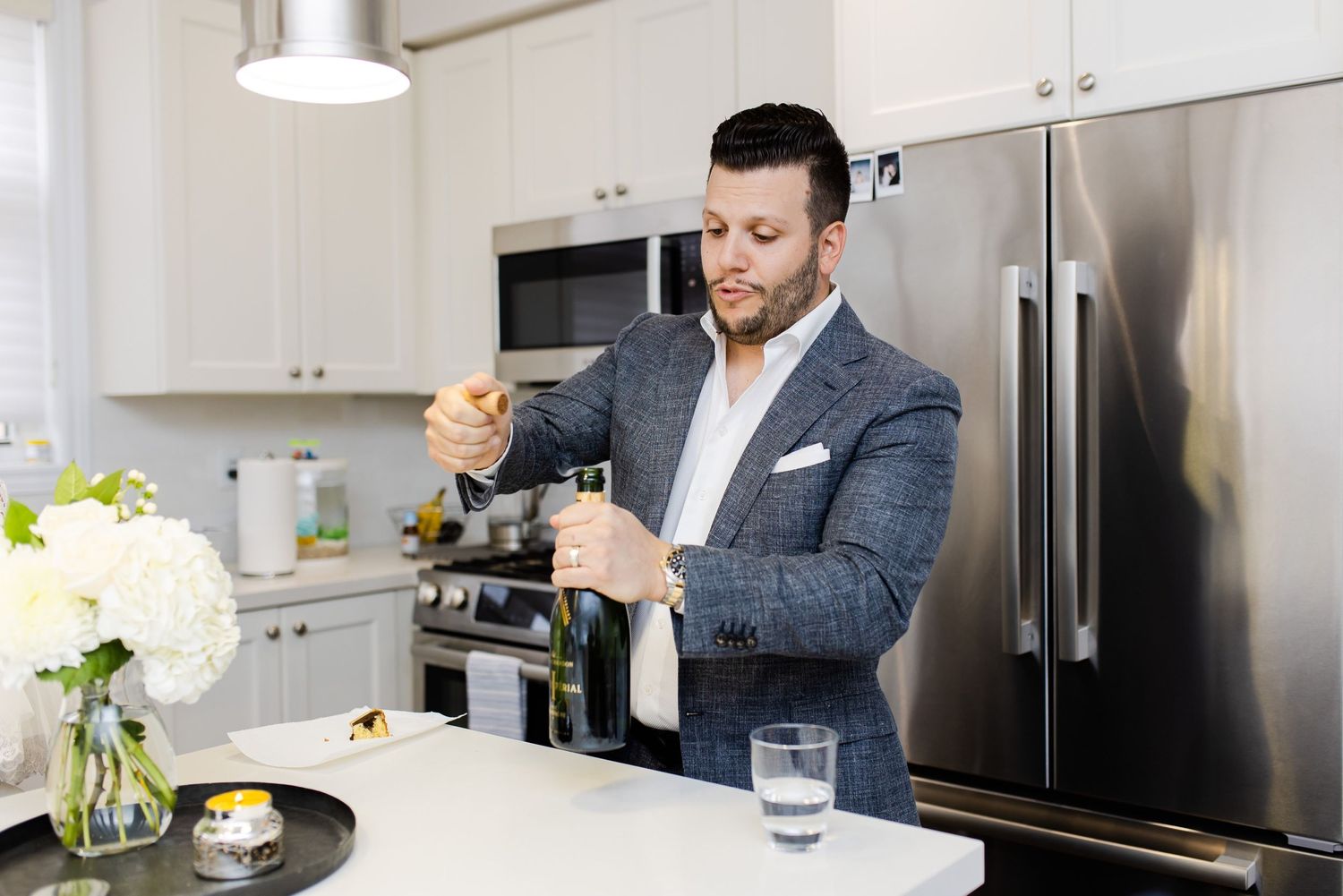 Man in grey suit jacket preparing drinks in modern kitchen.
